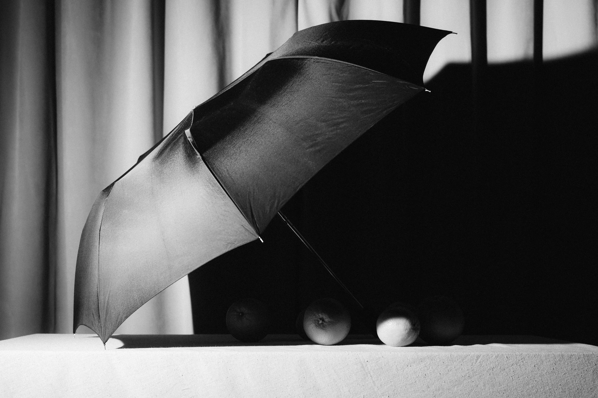 Oranges covered by an umbrella in black and white in front of velvet. I Used to Have Good Ideas #02 from Jonathan Grado's Saint Citrus series.