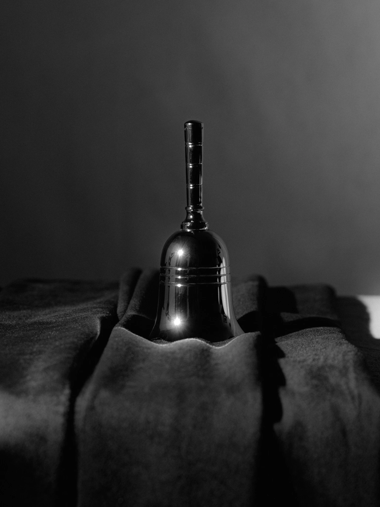 A small metallic hand bell on a velvet cloth in black and white. Selfie from Jonathan Grado's Saint Citrus series.