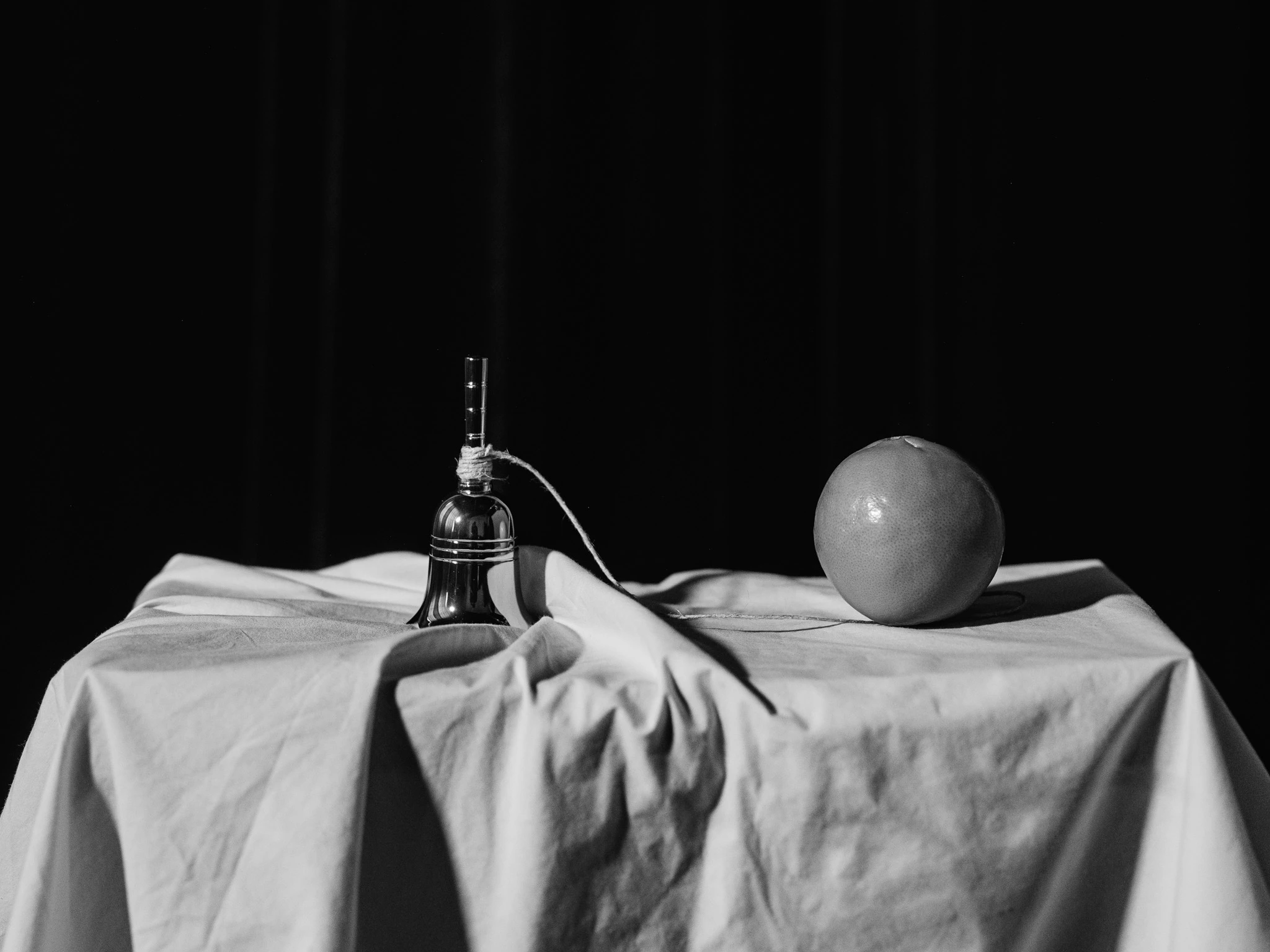 Hand bell and orange together conencted by a string. The Idea #03 from Jonathan Grado's Saint Citrus series.