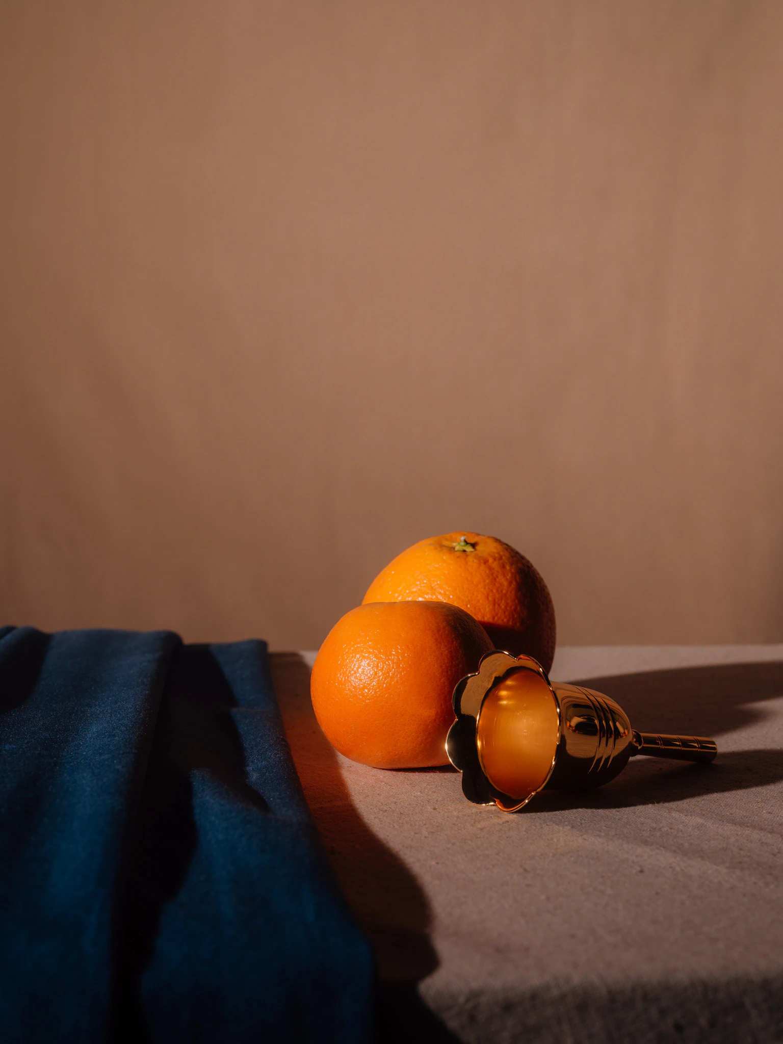 Two oranges with a small bell tilted over with blue and beige velvet. Vanity from Jonathan Grado's Saint Citrus series.