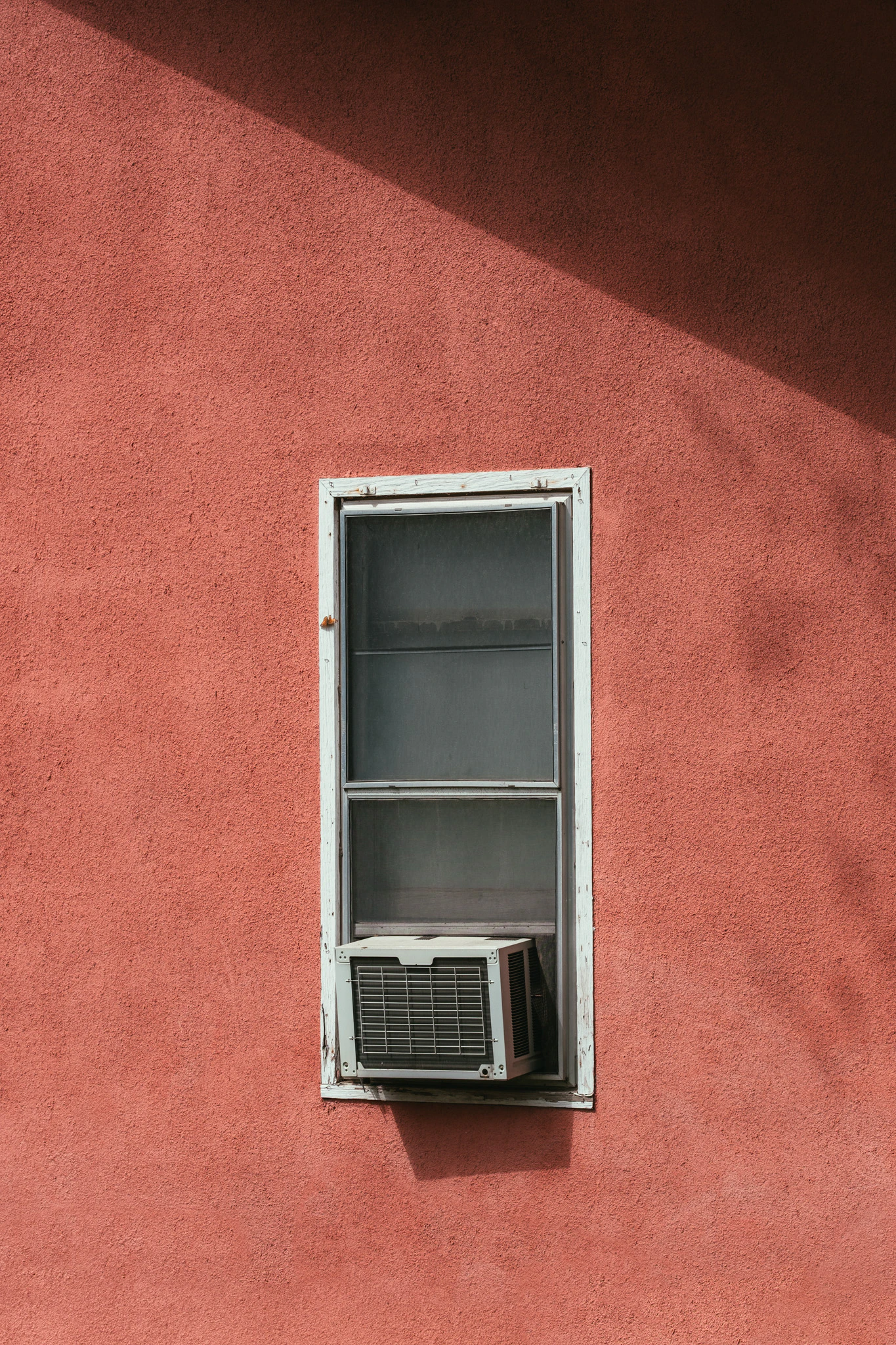 A single air conditioner unit in a pink walled window. Early August from Jonathan Grado's Provided You're Still Here series.