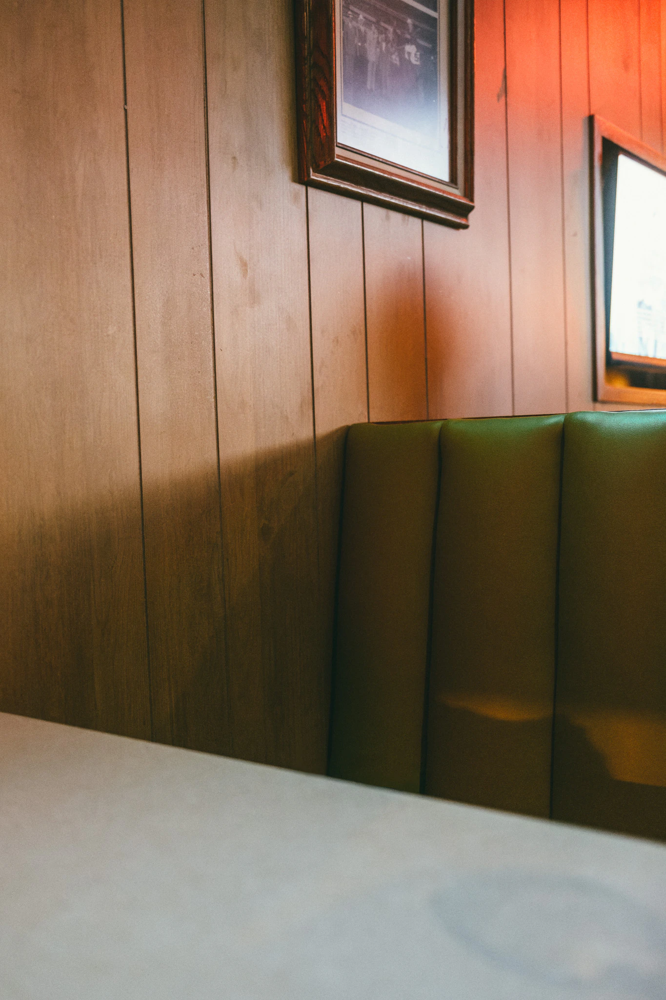 Empty green booth in a bar with a shadow of a person. Skinny's Off Track from Jonathan Grado's Provided You're Still Here series.