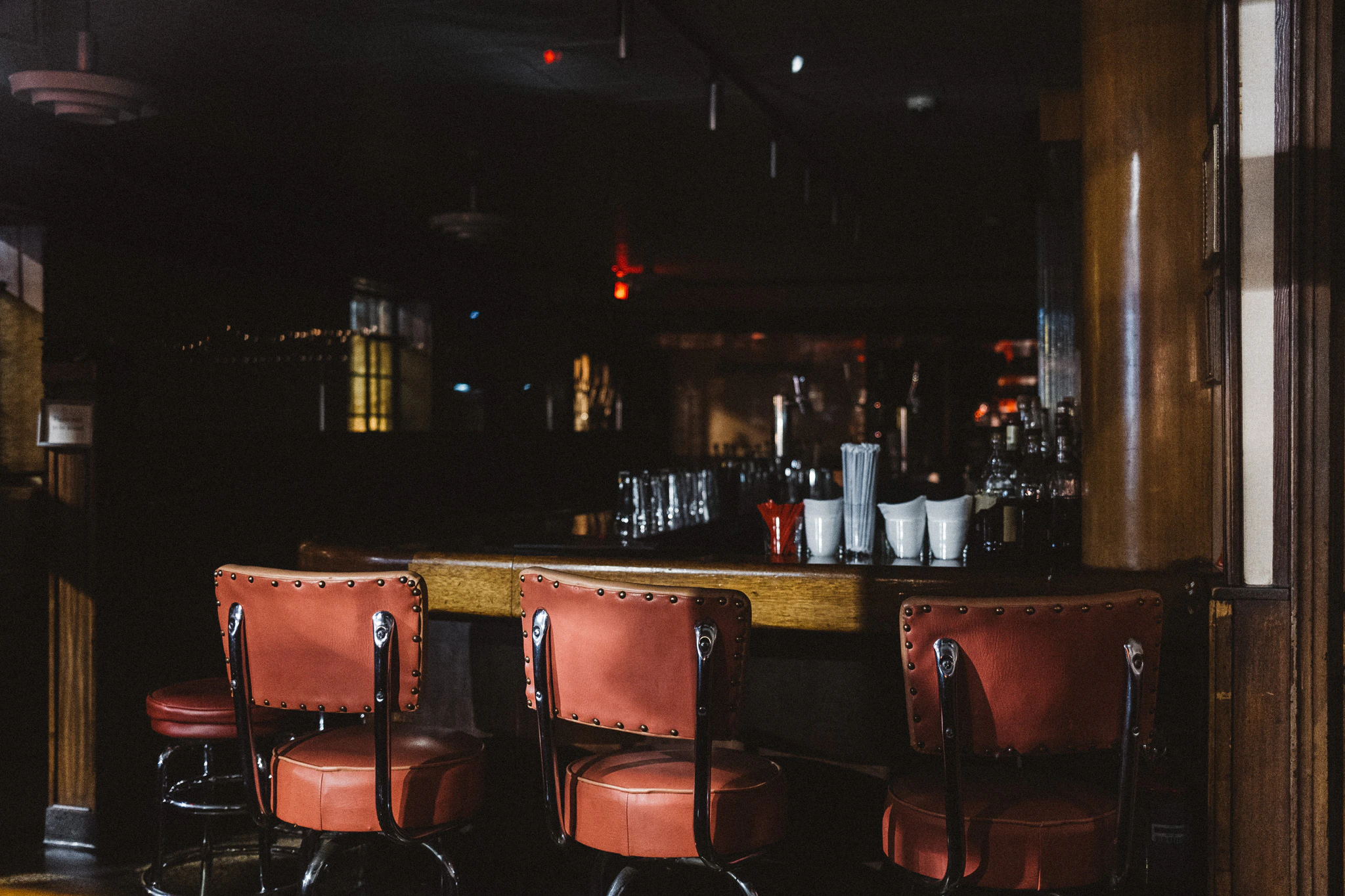 Three red leather bar stools in a dark and closed bar. From Jonathan Grado's Provided You're Still Here series.