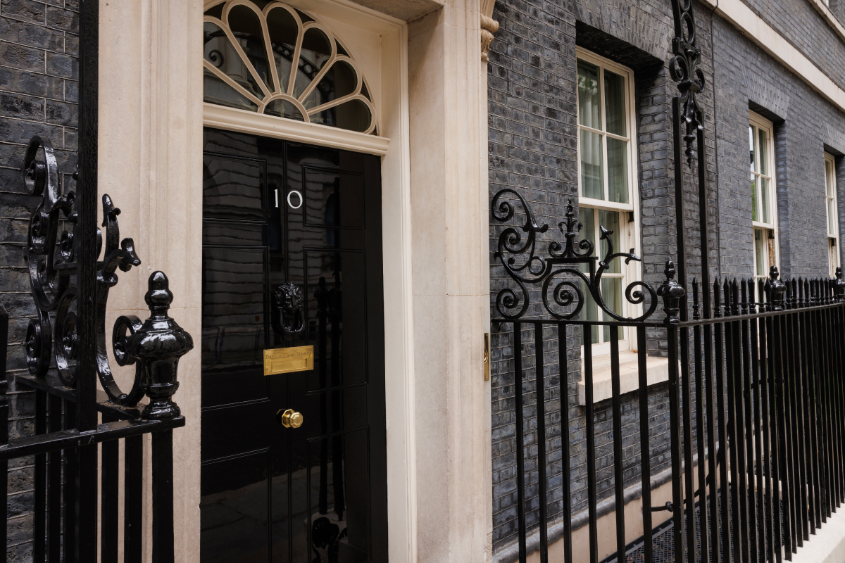 The entrance door of 10 Downing Street, London, featuring a black door with a gold plaque, surrounded by a wrought iron fence.