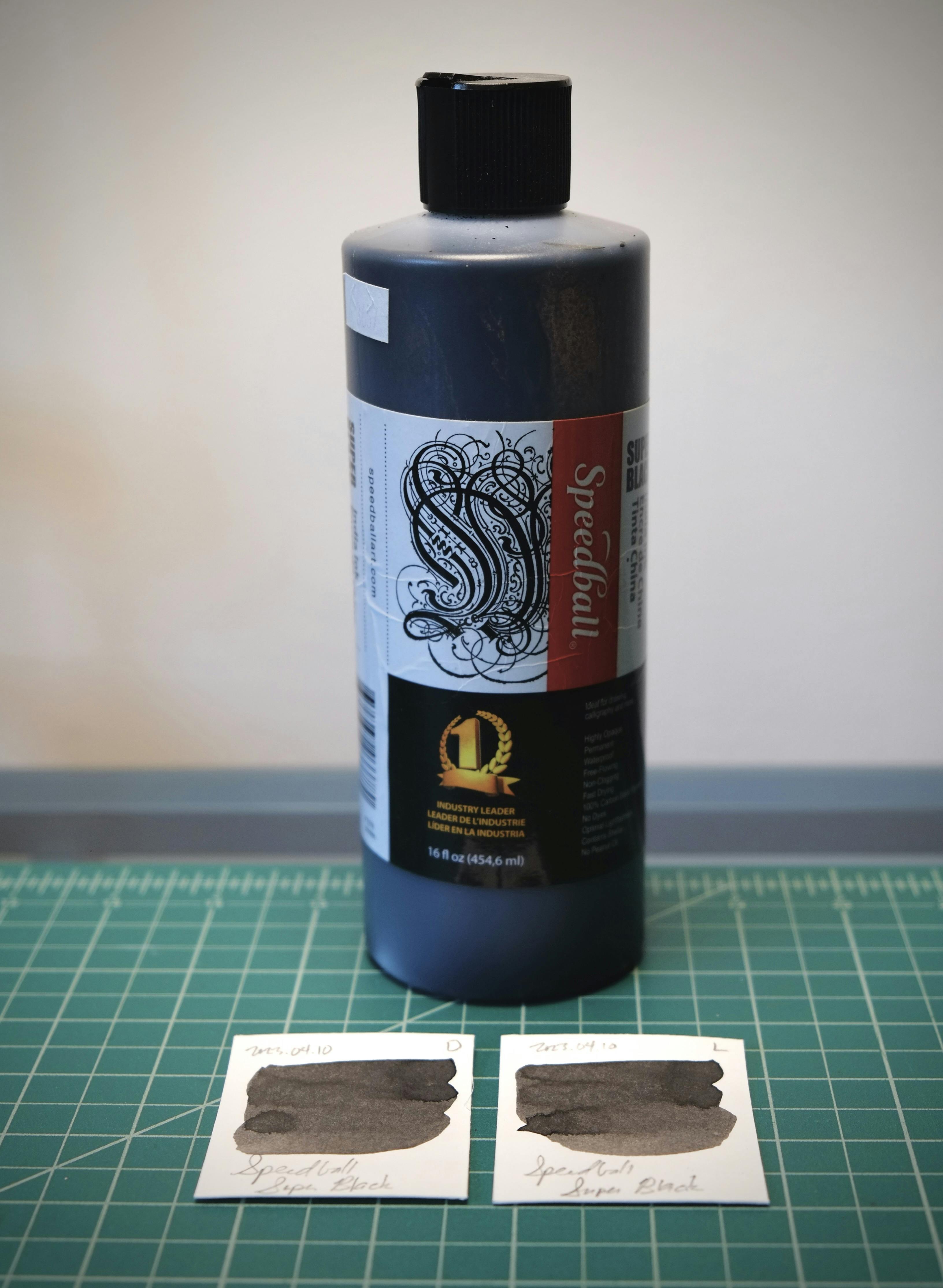 A bottle of Speedball Super Black India ink on a desk behind two color swatches