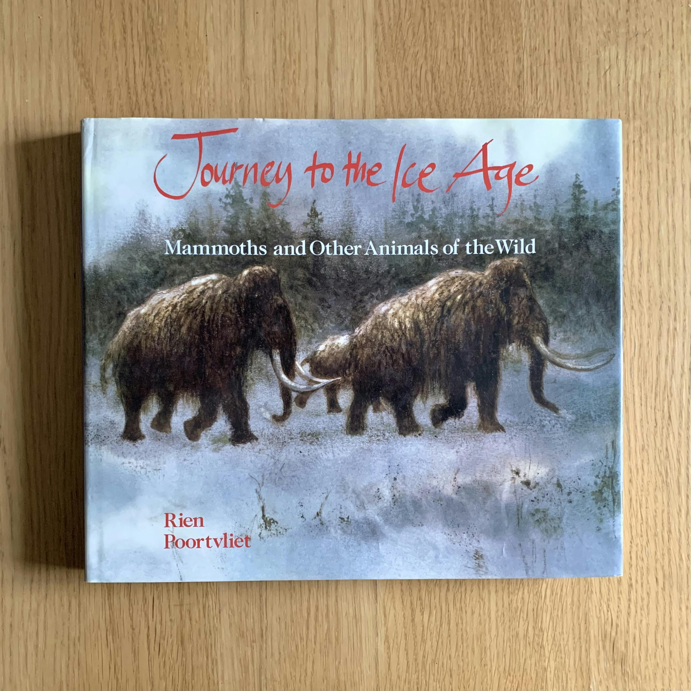 Cover of my copy of “Journey to the Ice Age” by Rien Poortvliet. The book rests on a wooden surface. The cover features a drawing of three mammoths walking in the snow in front of coniferous trees.