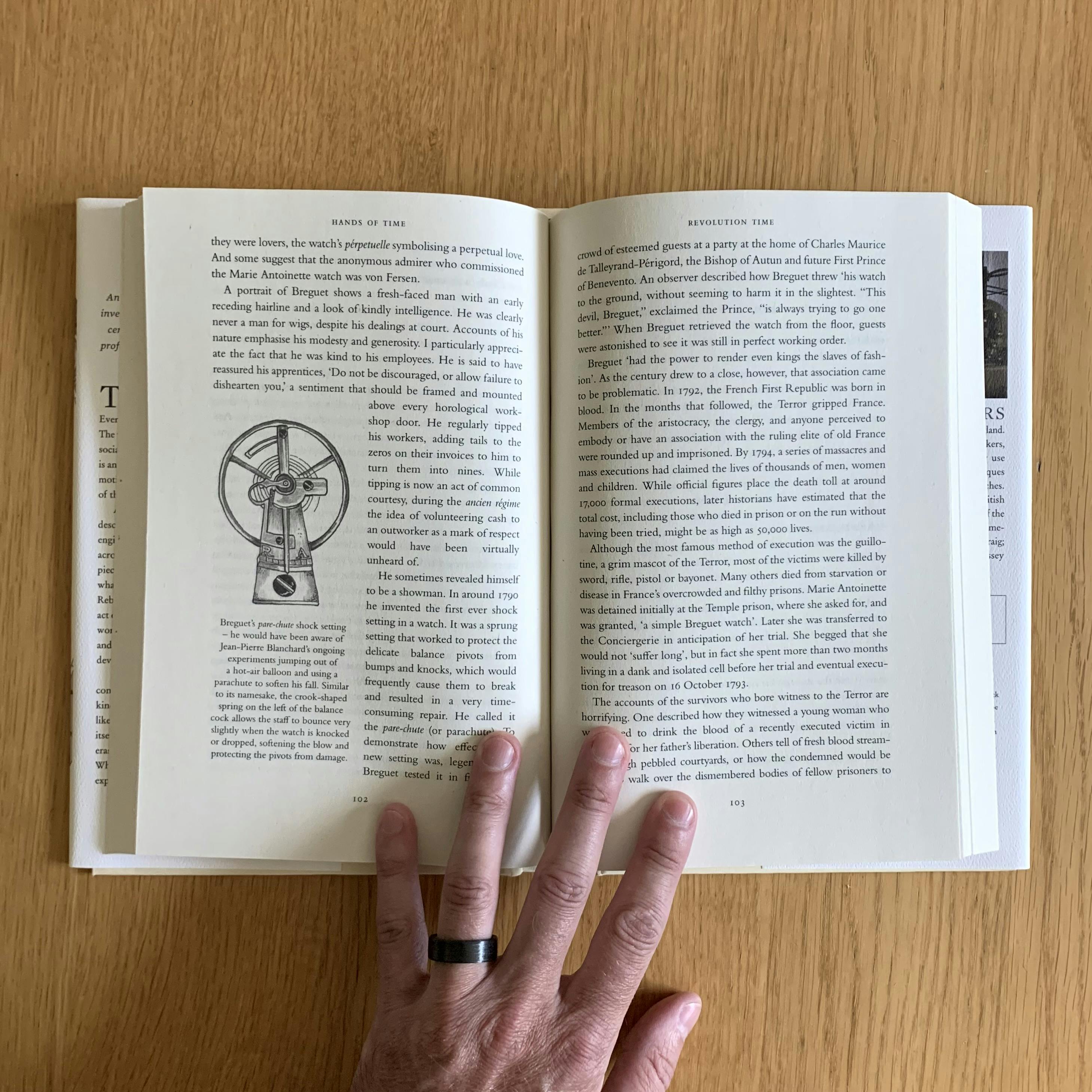 An inside spread of my copy of Rebecca Struthers’ Hands of Time. The books lays open on a wooden surface. An illustration of Breguet’s shock-protected balance cock, by Craig Struthers, is visible on the left-hand page.