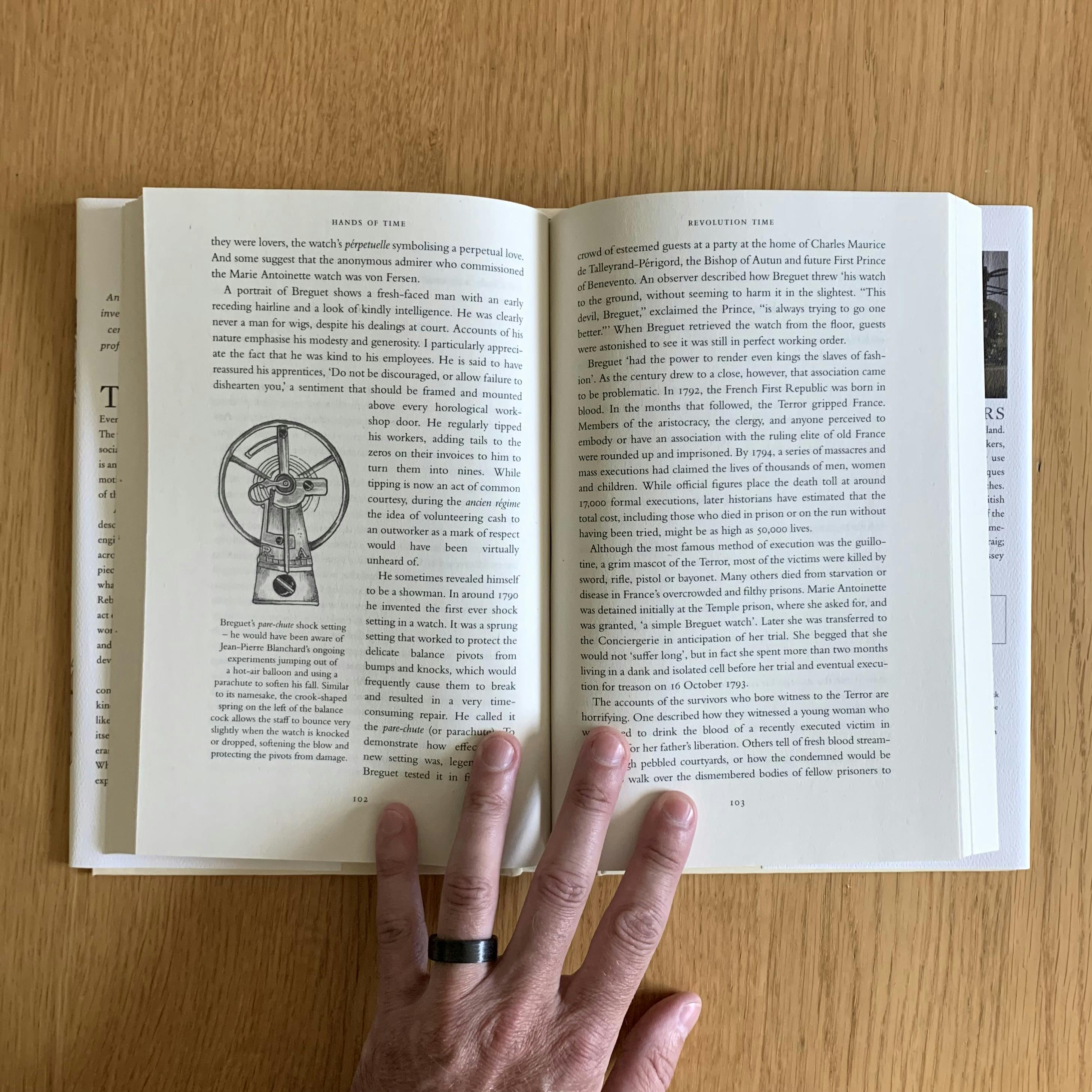 An inside spread of my copy of Rebecca Struthers’ Hands of Time. The books lays open on a wooden surface. An illustration of Breguet’s shock-protected balance cock, by Craig Struthers, is visible on the left-hand page.