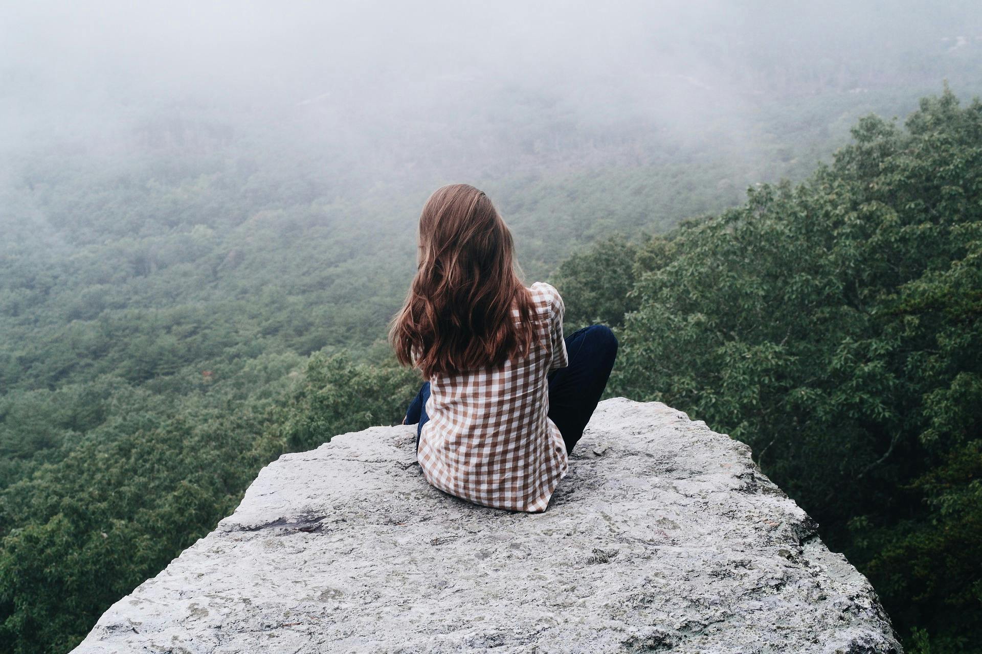A girl sitting on a cliff overlooking a forest
