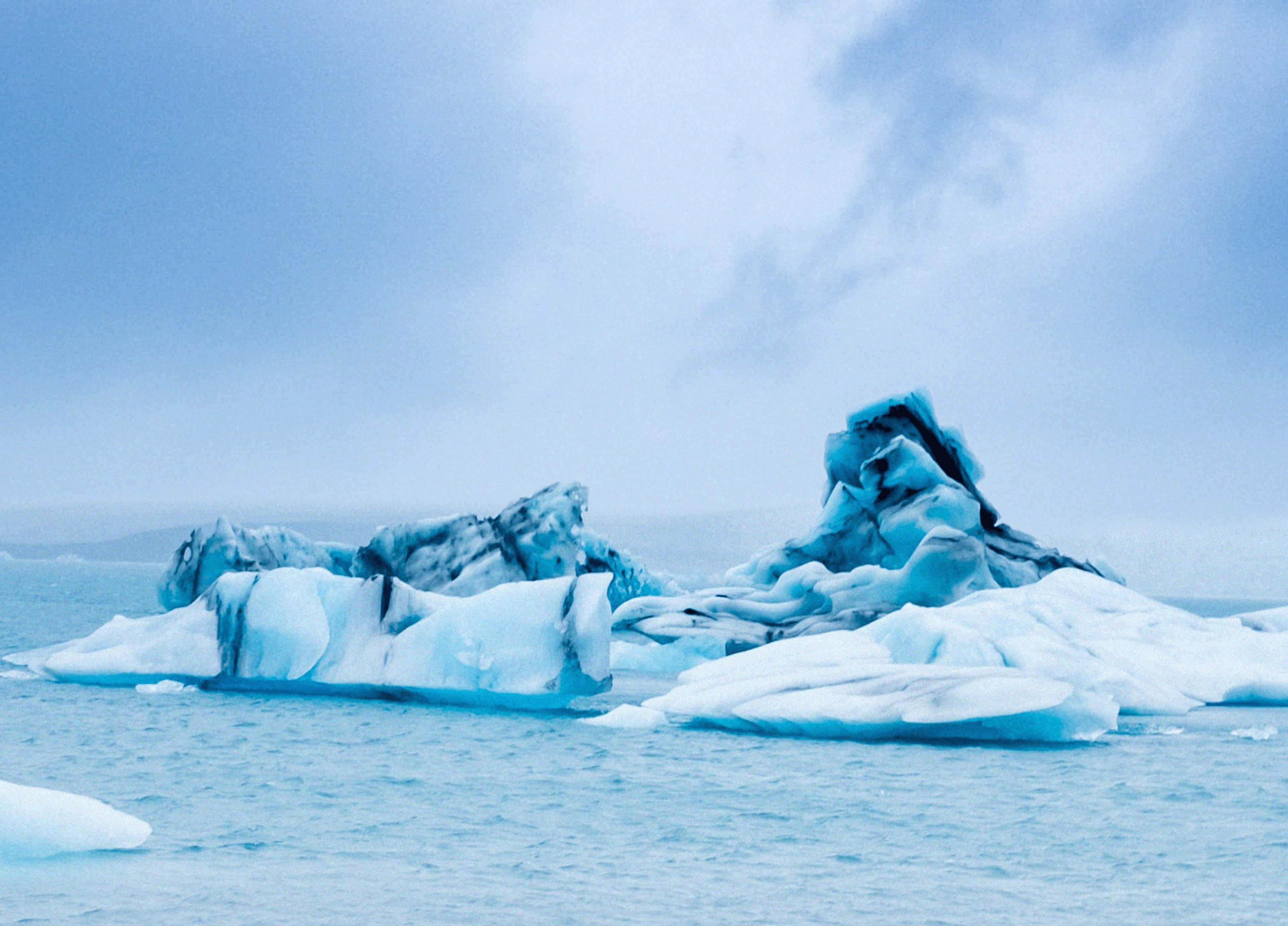 Ísbergsflotar á Íslandi fljóta á rólegu bláu hafi undir skýjuðu lofti, sem skapar friðsæla og kaldan stemningu.