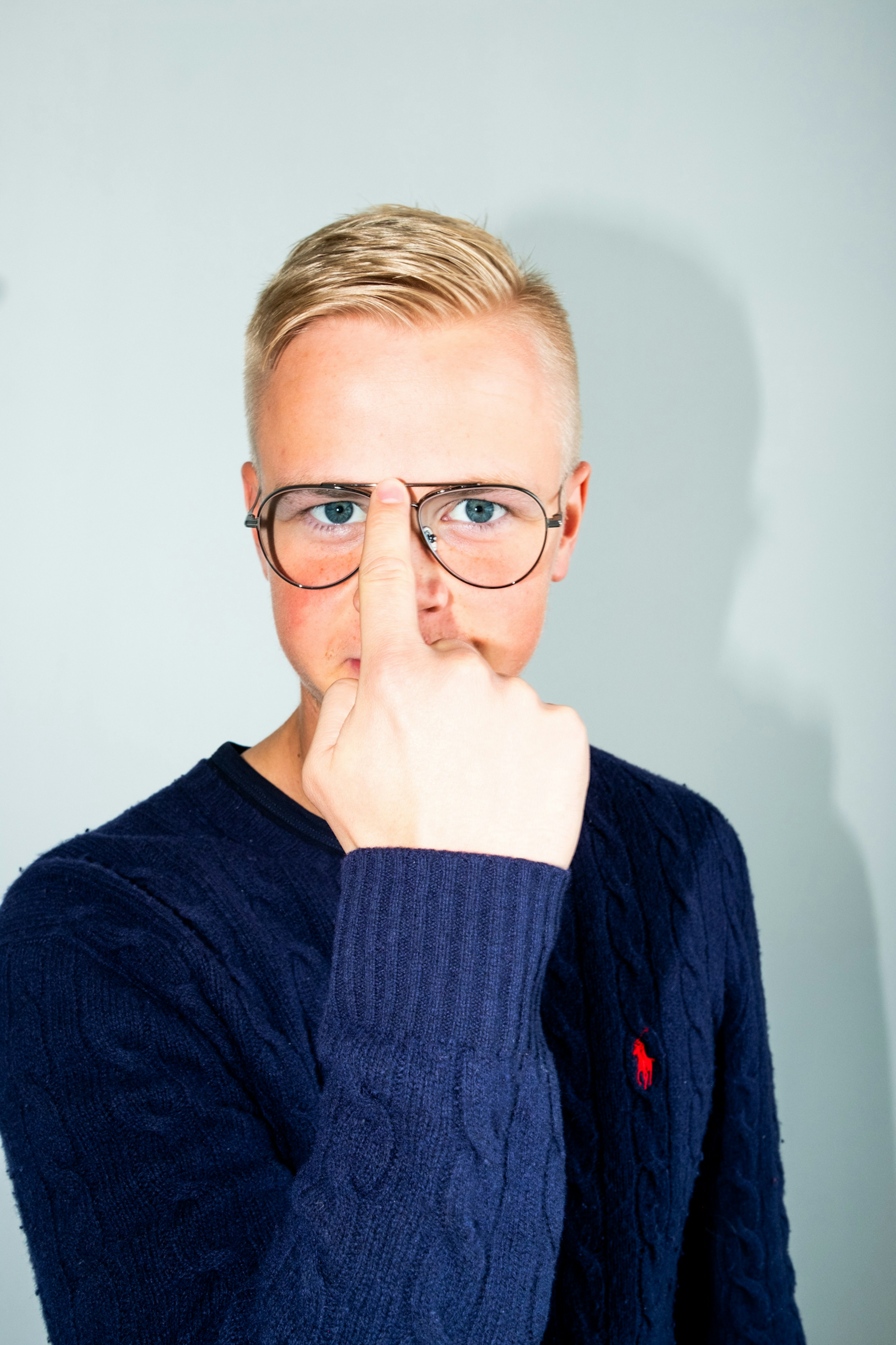 Starfsmaður Júní með stutt ljóst hár og gleraugu stillir gleraugun sín leikandi með fingrinum, klæddur í dökkbláan peysu á ljósgráum bakgrunni.