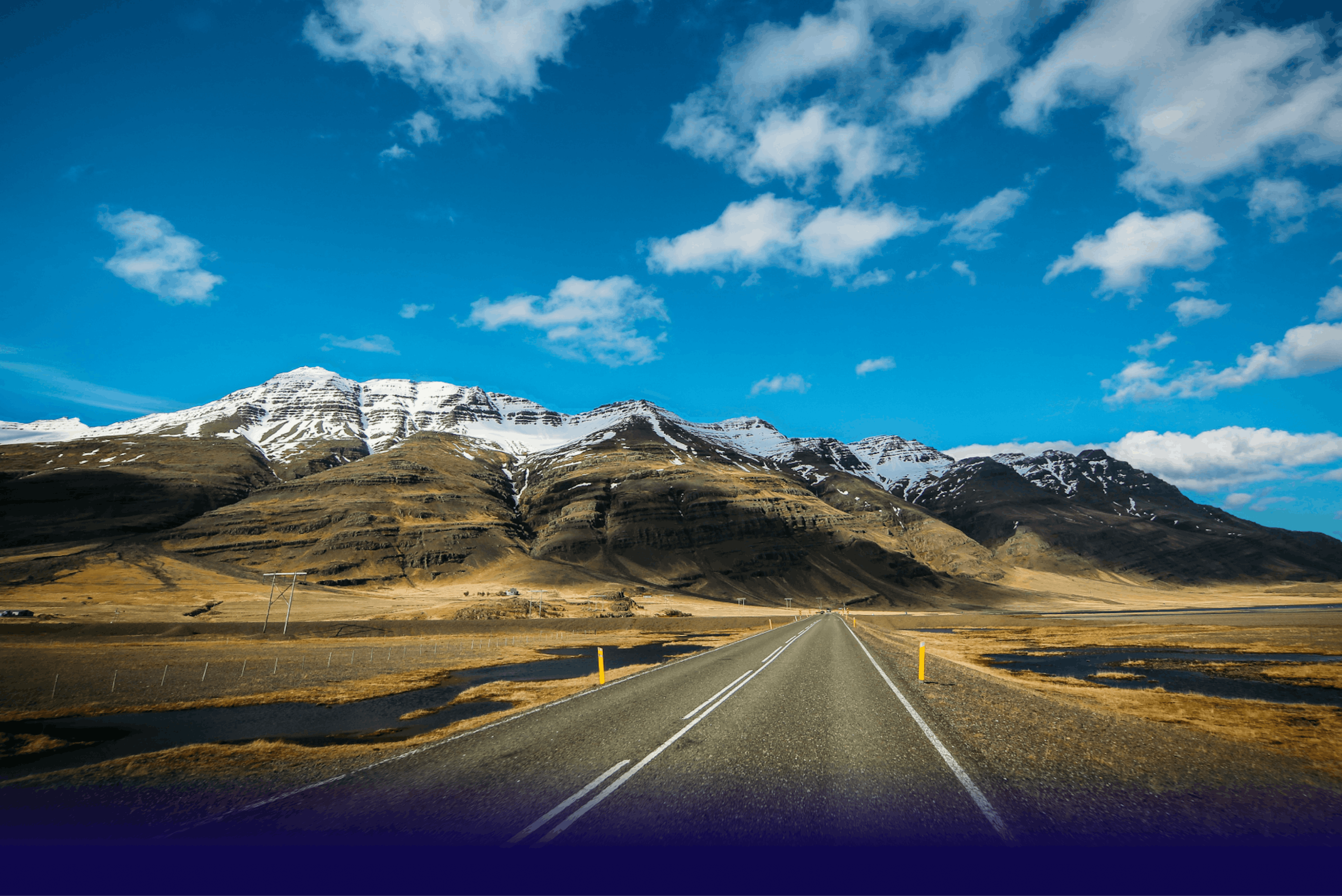 Leið til snæviþöktra fjalla undir björtum bláum himni á Íslandi.