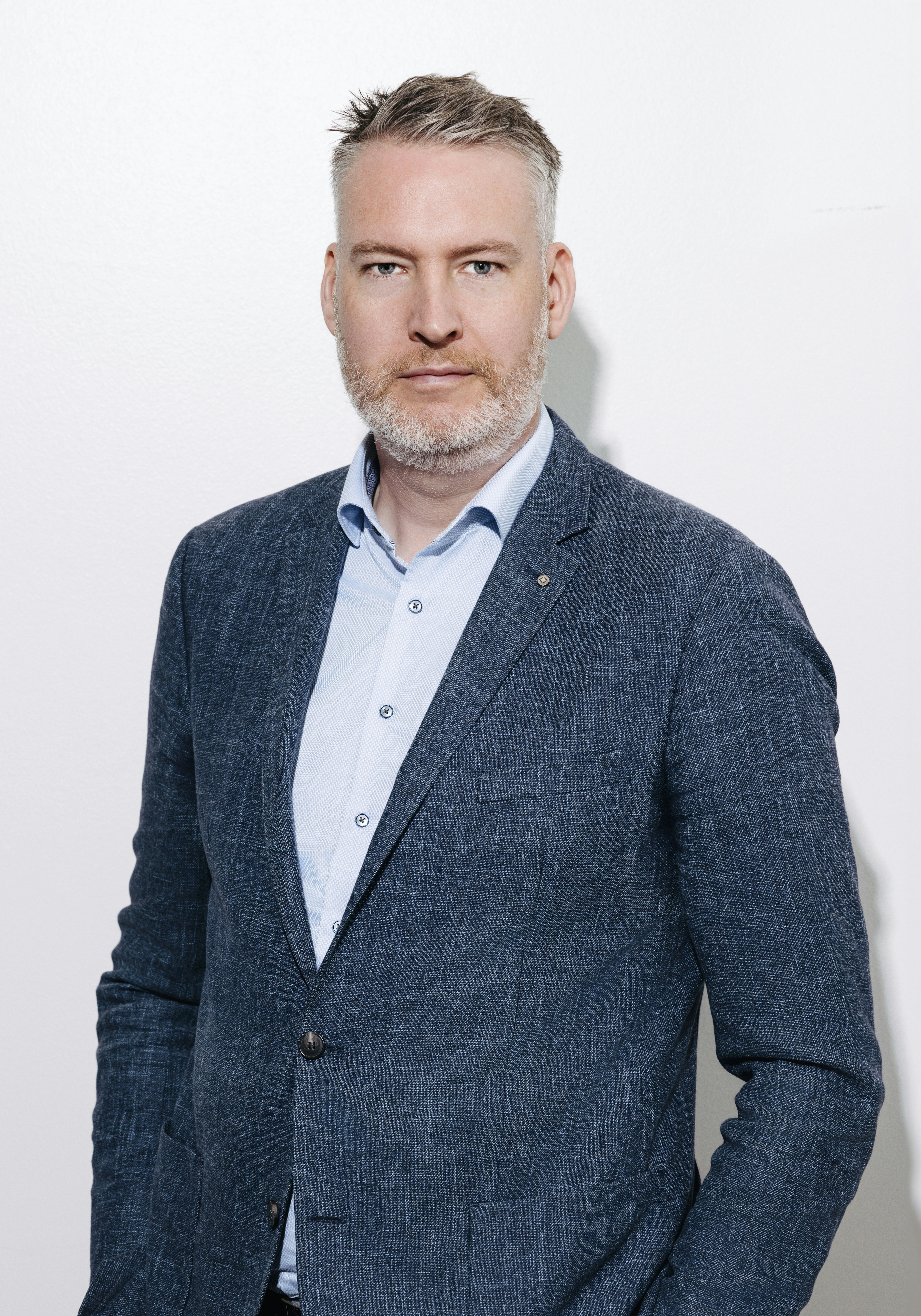Maður með stutt, greitt hár og skegg er í bláum jakkafötum yfir ljósbláum skyrtu.