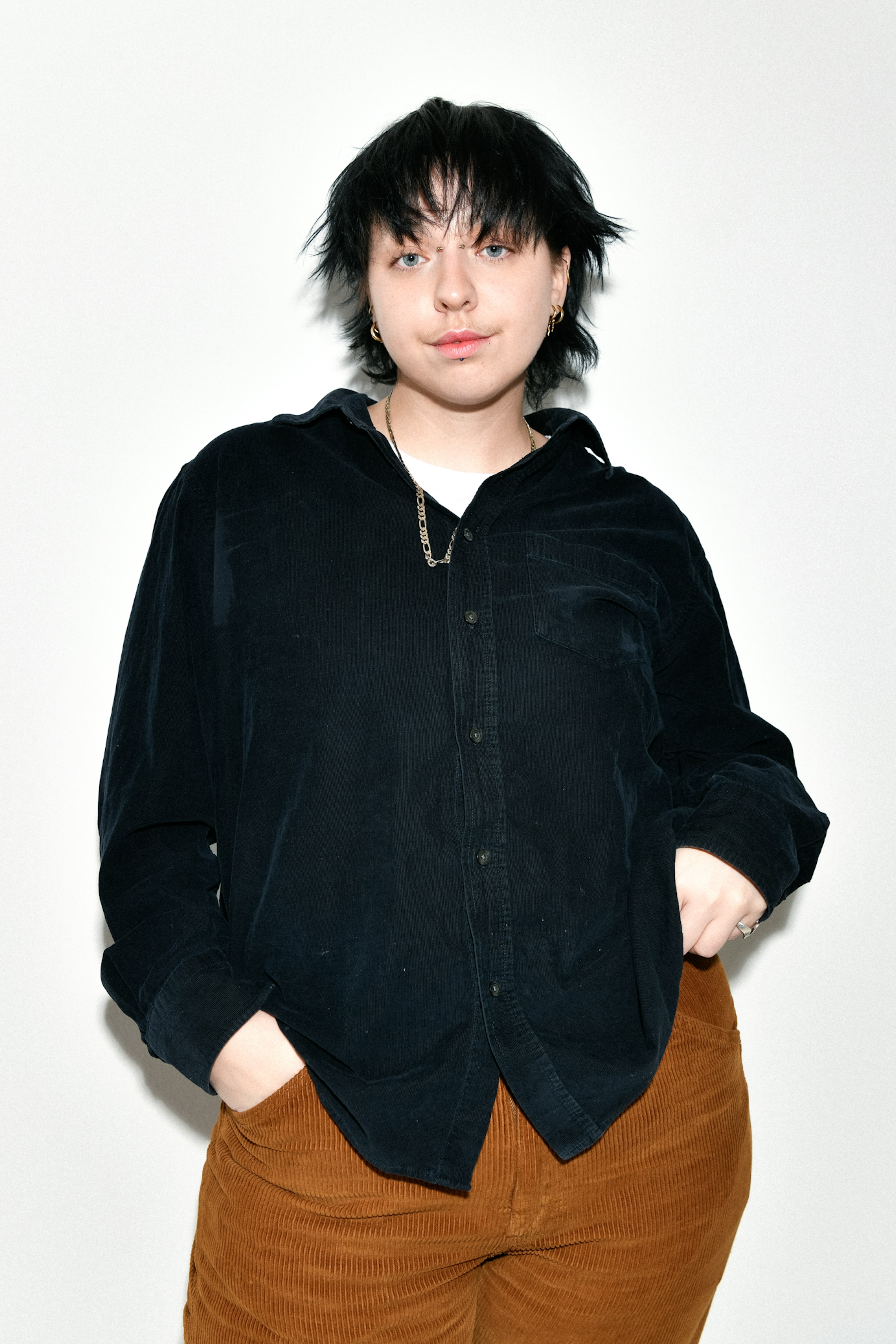 Einstaklingur með stutt, ruglað svart hár stendur fyrir framan hvítan bakgrunn.