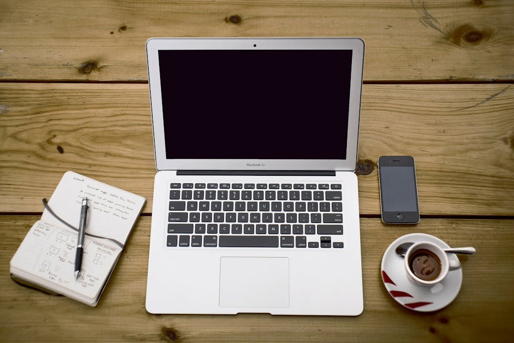 Photo of desk with coffee, phone, laptop and notepad