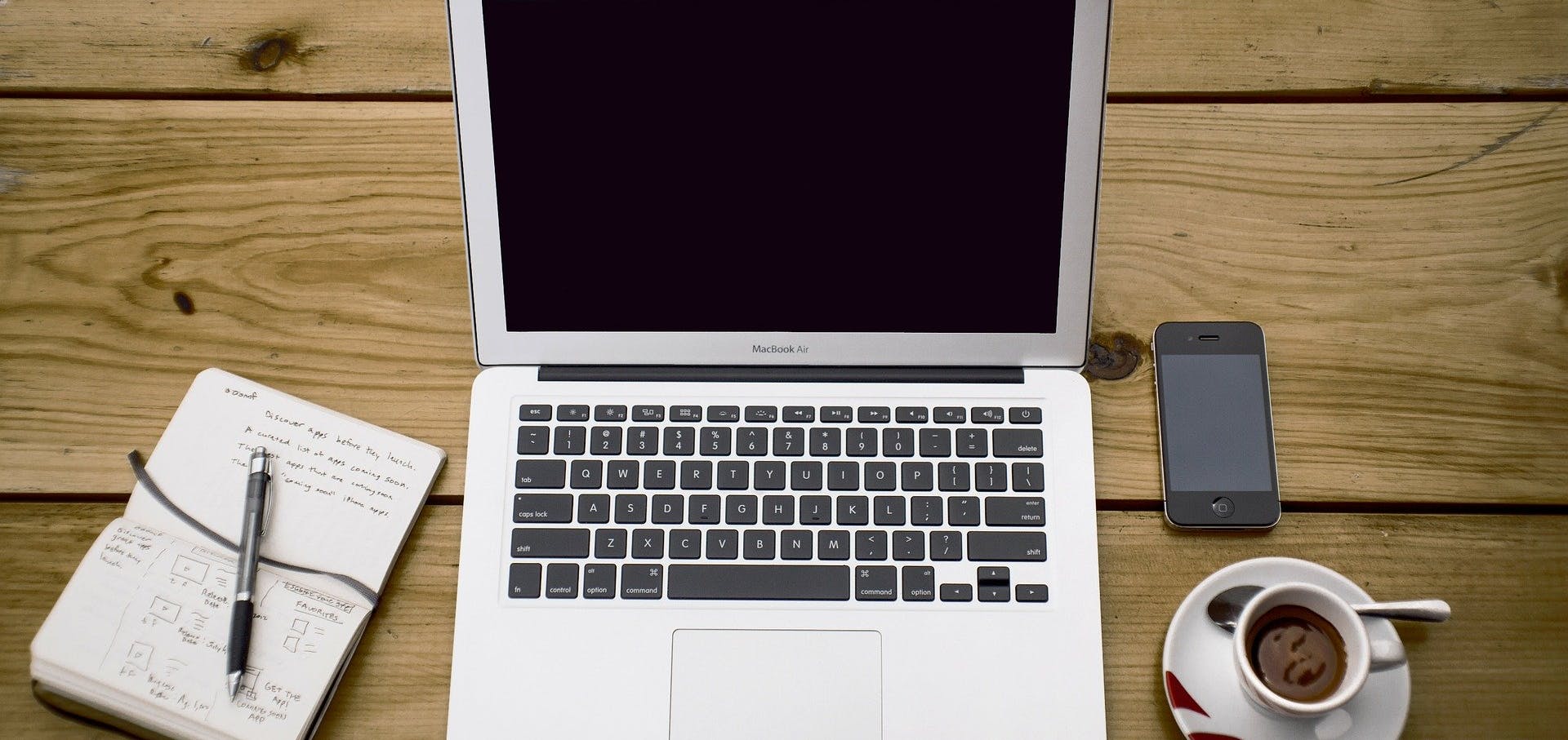 Photo of desk with coffee, phone, laptop and notepad