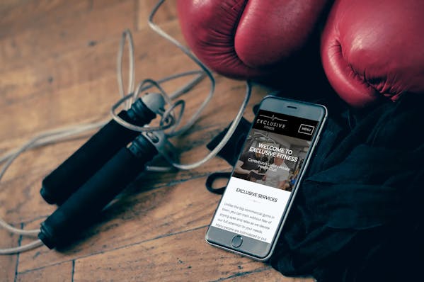 Exclusive Fitness website on iPhone 8 surrounded by gym equipment