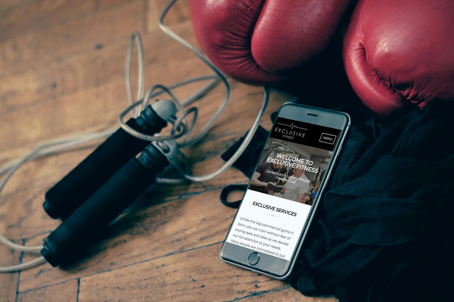 Exclusive Fitness website on iPhone 8 surrounded by gym equipment