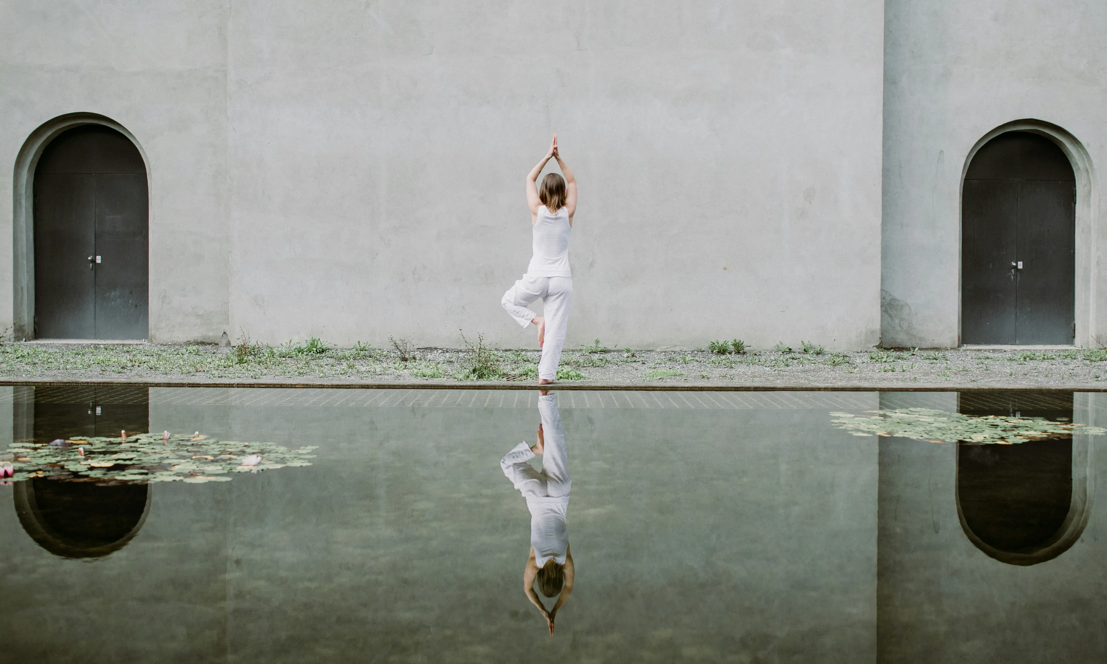 woman balancing on one foot with reflection at edge of pond
