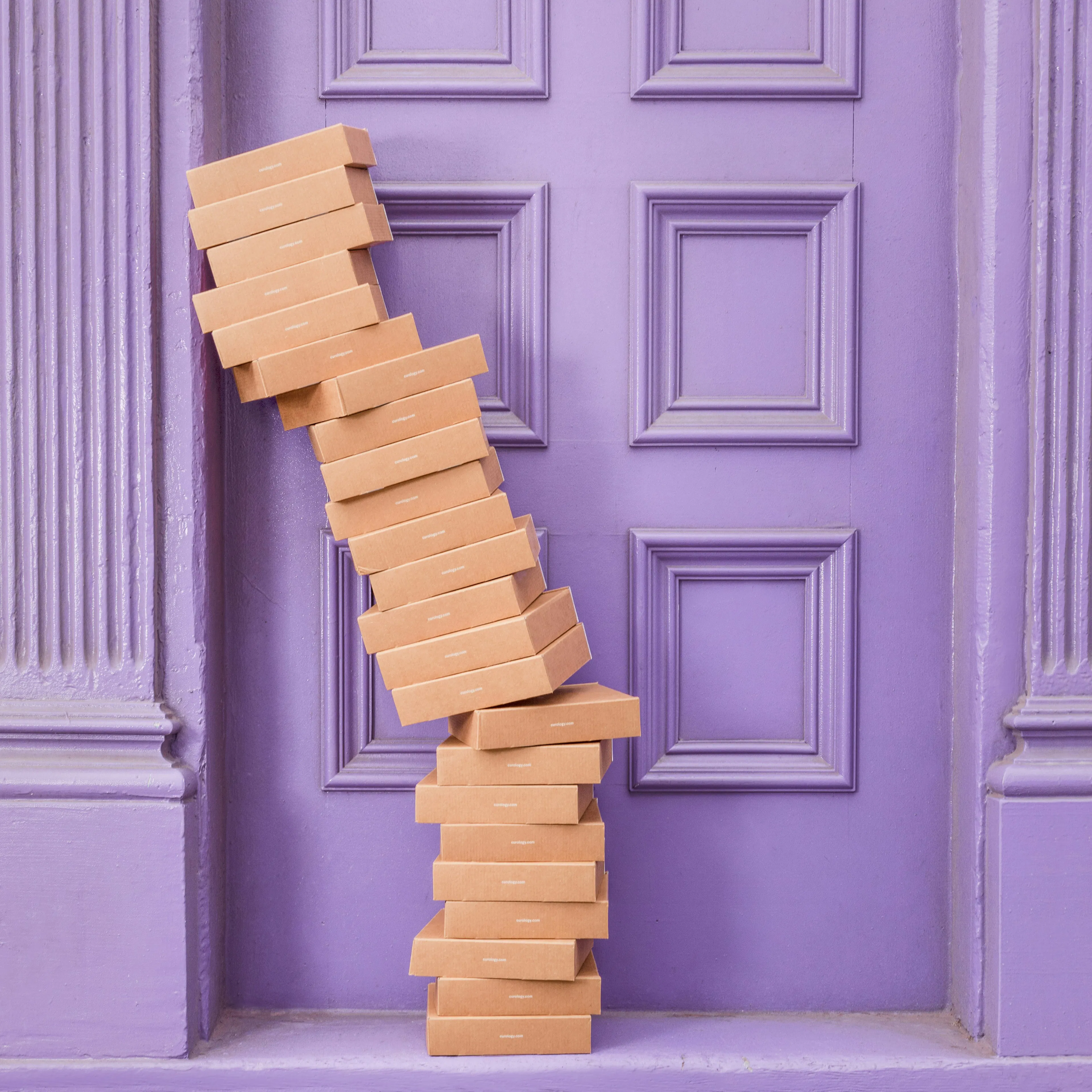 a stack of boxes leaning to the left in front of a lavender doorway