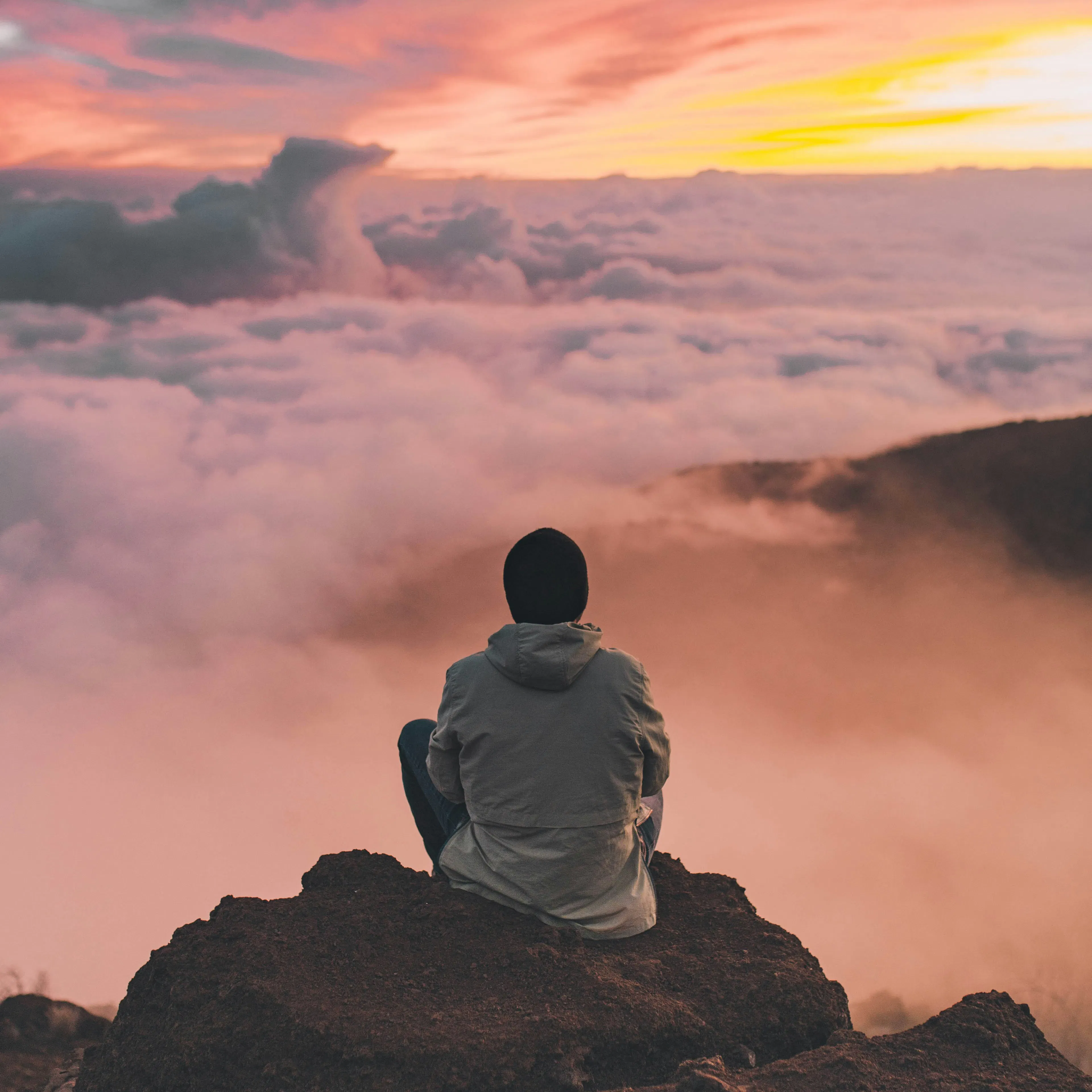 man sits at a mountain top over rolling clouds