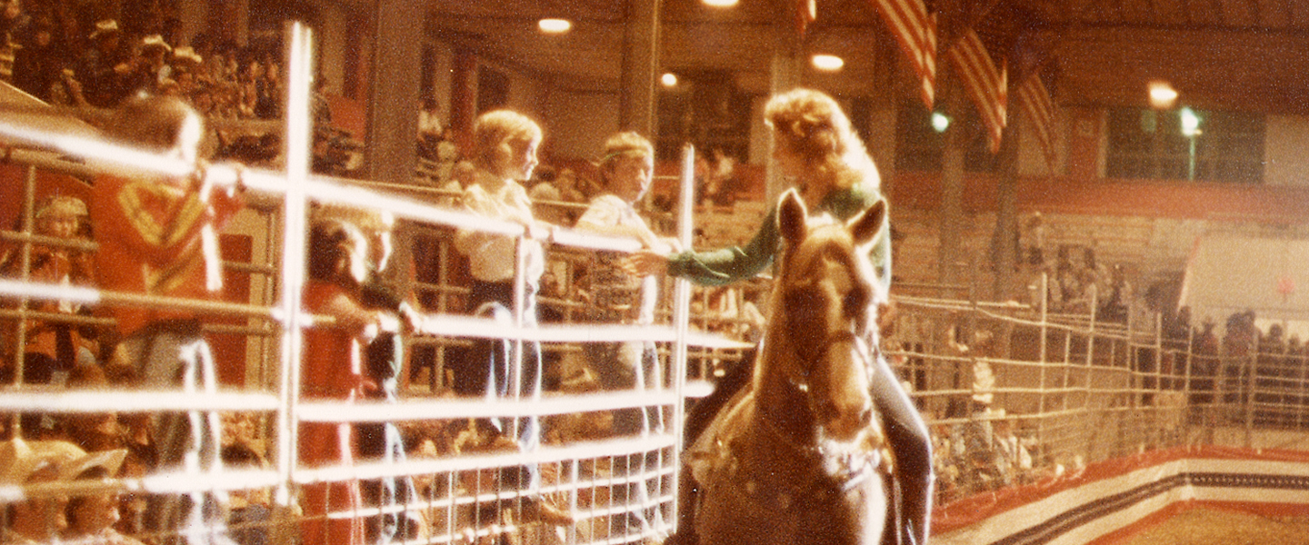 A picture of Reba on her horse talking to kids at a rodeo.