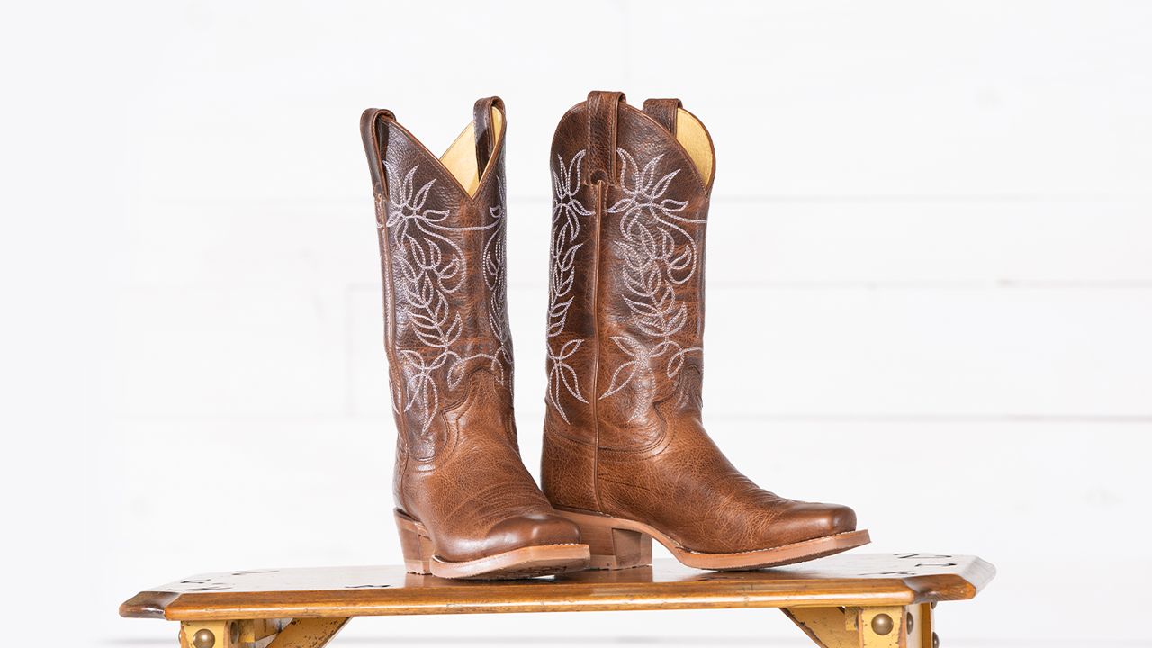 A pair of brown boots stand on a table in front of a white background.