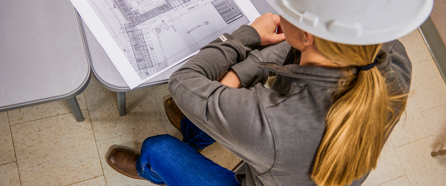 Woman looking at blue prints on table in brown cowgirl boots.