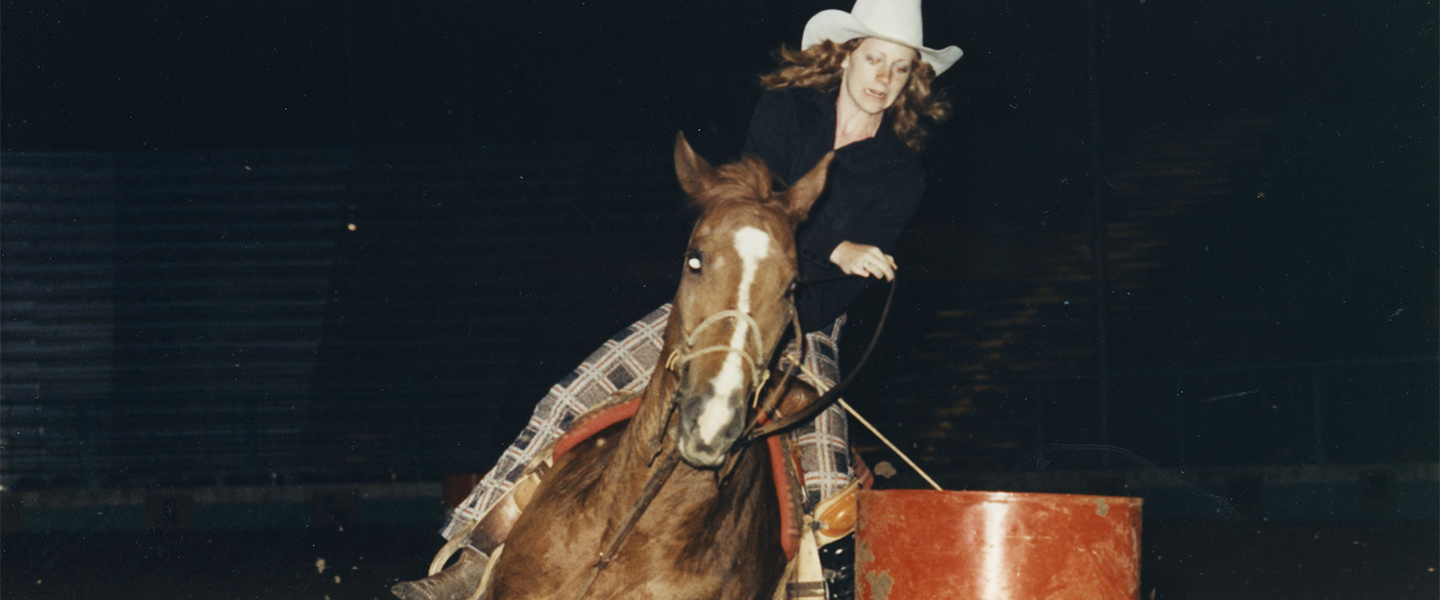 A picture of Reba McEntire on her horse in a barrel racing event.