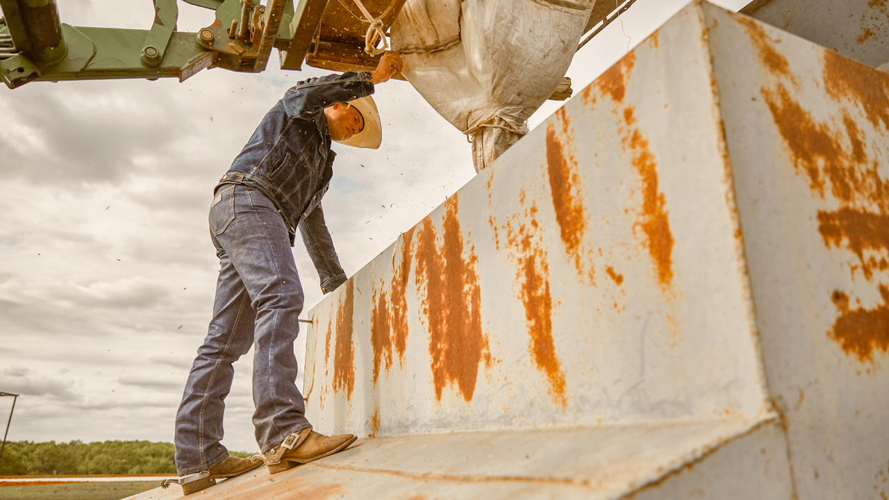 Professional Bull Fighter Cody Webster loading livestock feed into a feeder from a tractor.