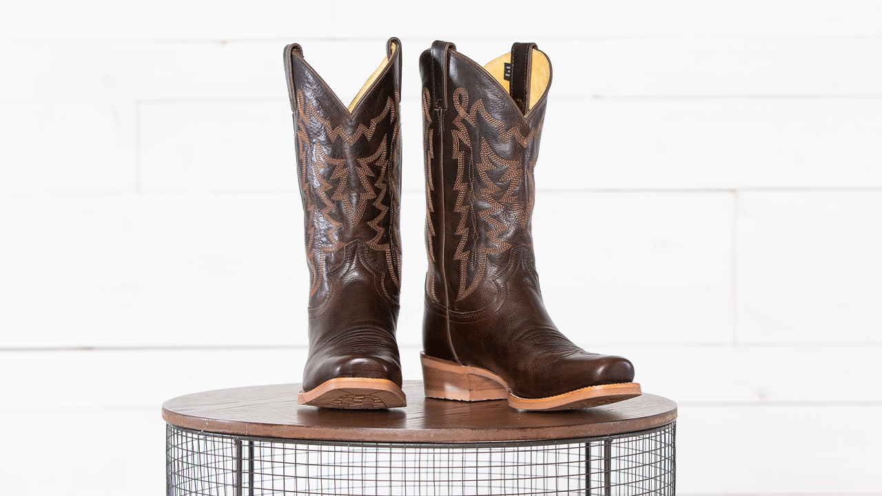 Las botas de piel de vaca marrón oscuro de la colección Justin Classics destacan sobre un fondo blanco.