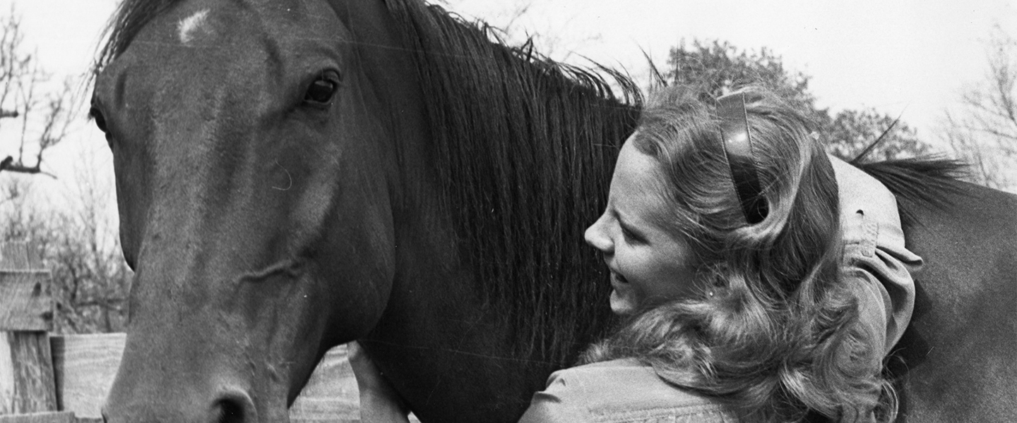 An old black and white picture of young Reba McEntire with her horse.