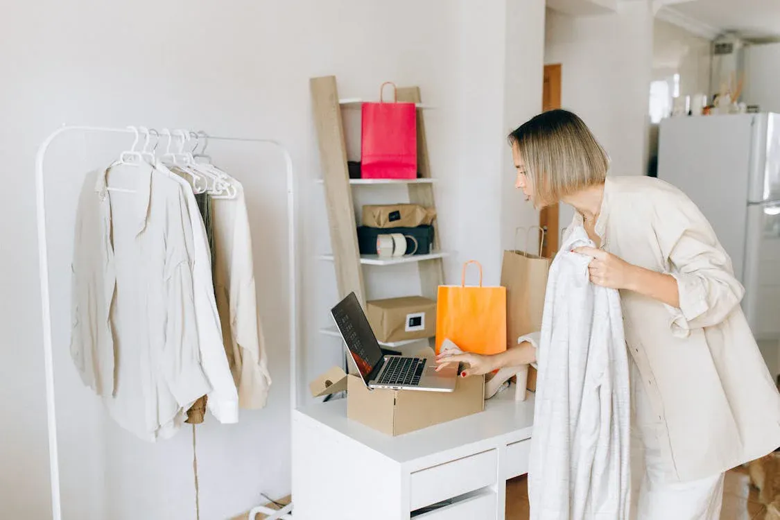 Woman holding some clothes and typing into her laptop