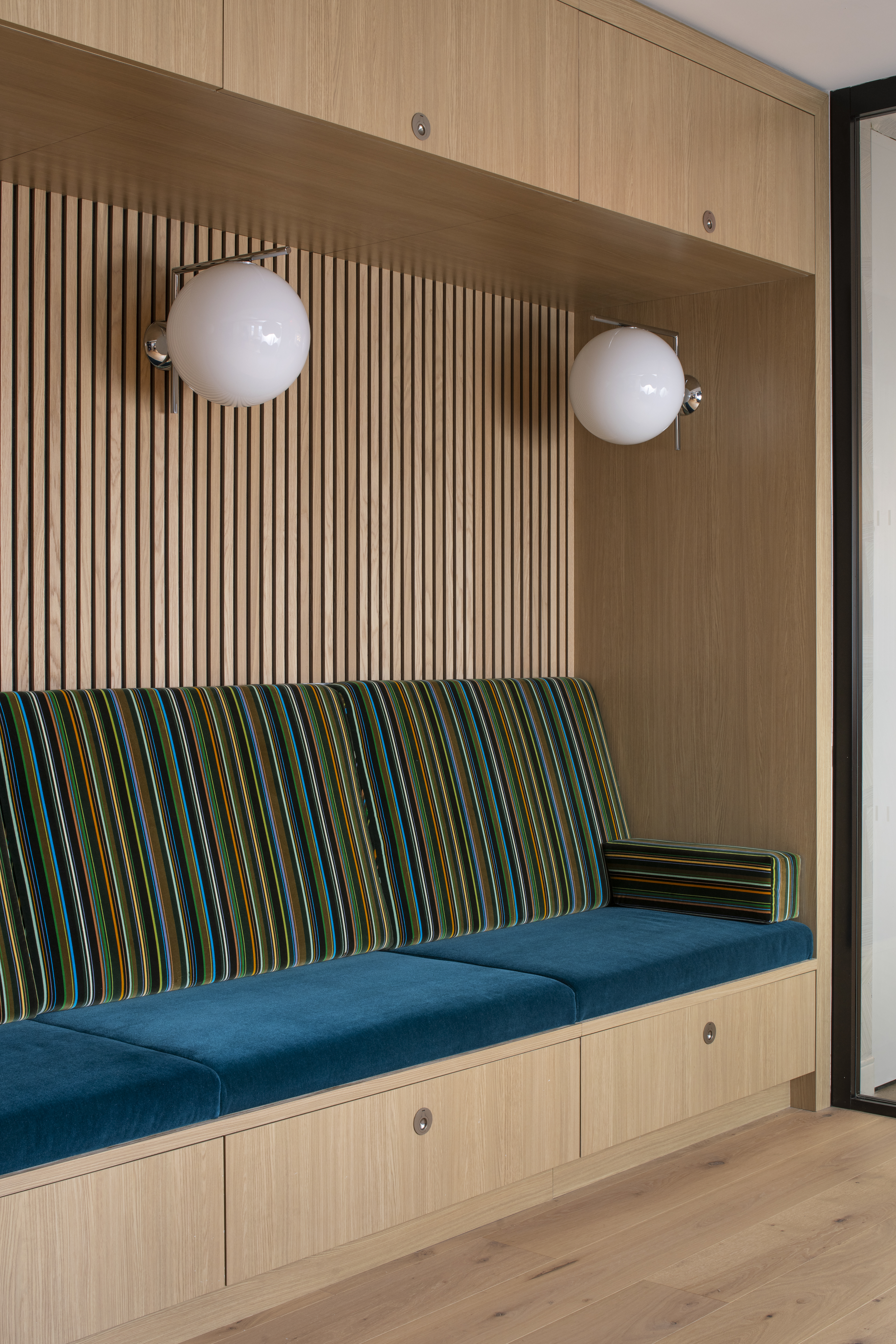 Custom built-in bench at One Penn Plaza by K.A. Murphy Interiors featuring oak millwork, teal velvet seating, striped upholstery, and integrated storage.