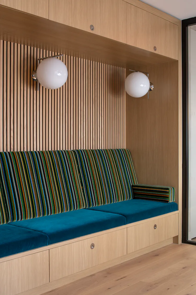 Custom built-in bench at One Penn Plaza by K.A. Murphy Interiors featuring oak millwork, teal velvet seating, striped upholstery, and integrated storage.