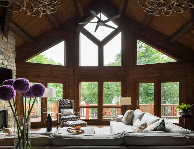 Spacious family room in a Hudson Valley log cabin featuring a double-height stone fireplace, vaulted wood ceilings, and expansive windows, designed by K.A. Murphy Interiors.