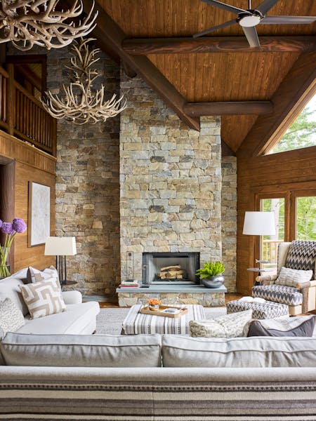 Spacious family room in a Hudson Valley log cabin featuring a double-height stone fireplace, vaulted wood ceilings, and expansive windows, designed by K.A. Murphy Interiors.