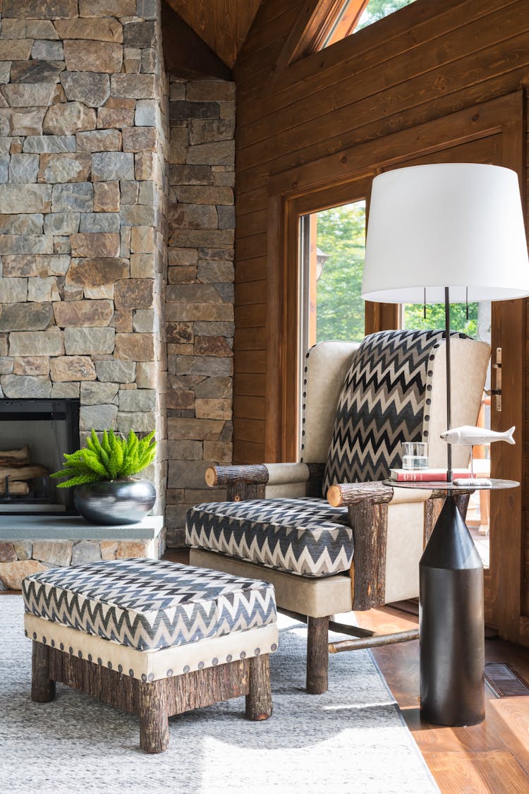 Inviting corner chair in a Hudson Valley log cabin’s family room, offering a cozy reading nook with natural light, designed by K.A. Murphy Interiors