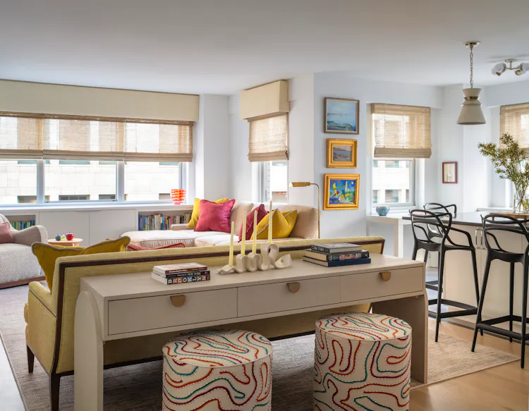 Colorful Greenwich Village living and dining area featuring a yellow sofa, patterned ottomans, layered artwork, and custom furnishings by K.A. Murphy Interiors.