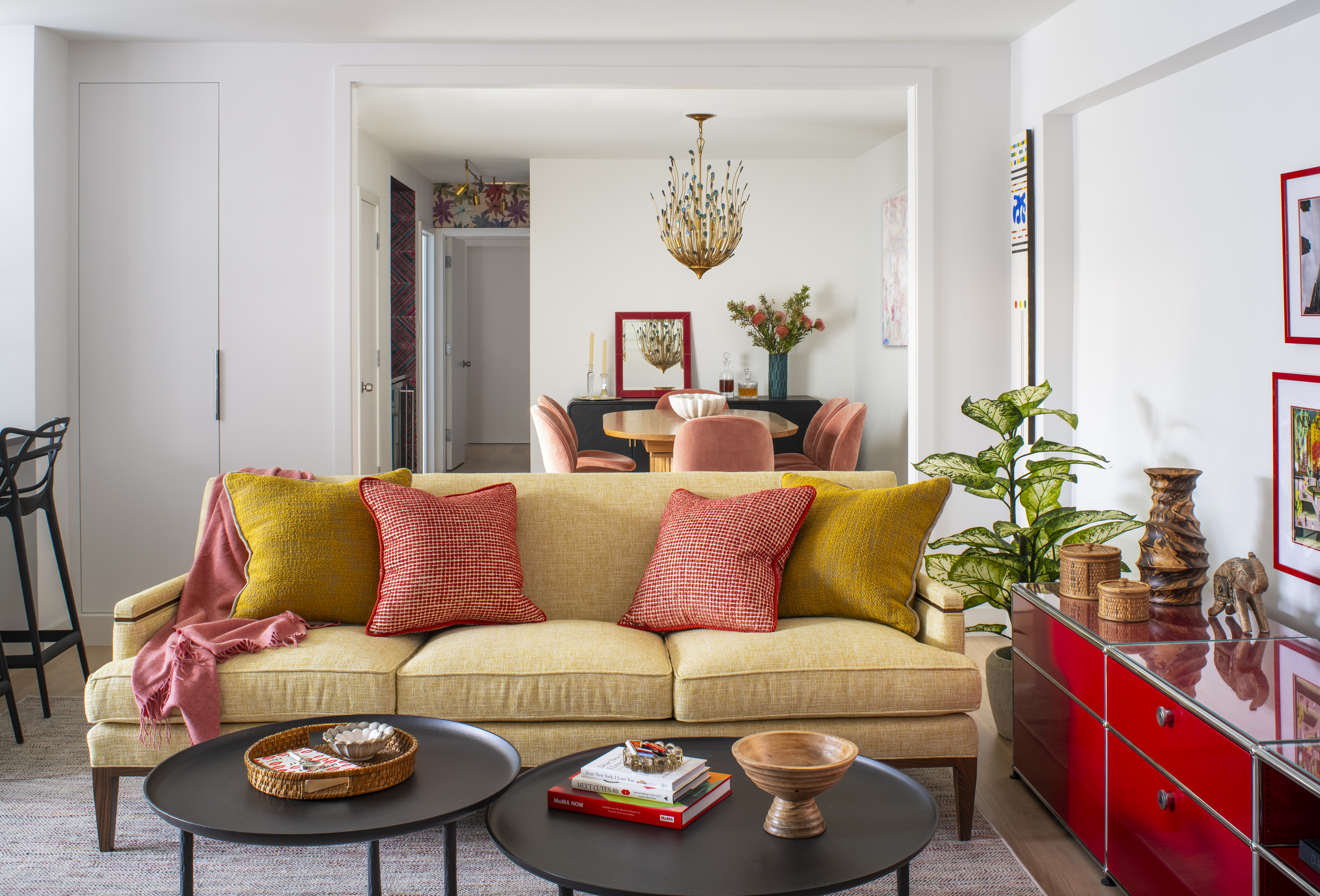 Greenwich Village living room with a yellow sofa, layered pillows, and a bold red console opening into a colorful dining area by K.A. Murphy Interiors.