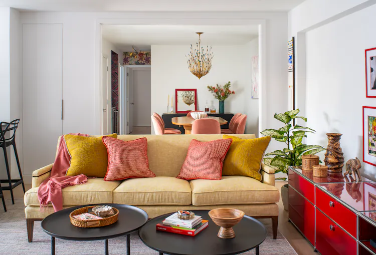 Greenwich Village living room with a yellow sofa, layered pillows, and a bold red console opening into a colorful dining area by K.A. Murphy Interiors.