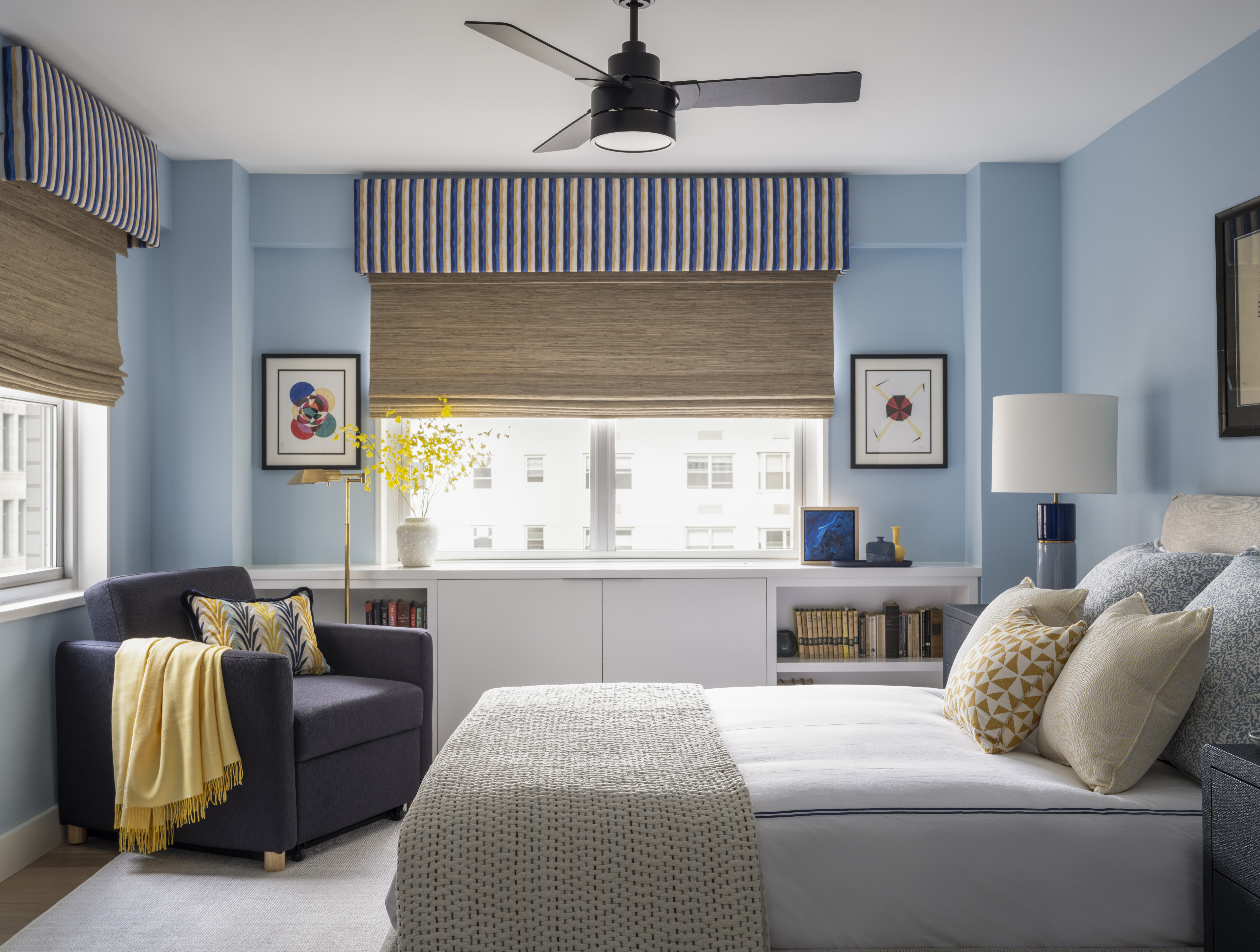 Guest bedroom with soft blue walls, layered bedding, custom window treatments, and a reading chair by K.A. Murphy Interiors.