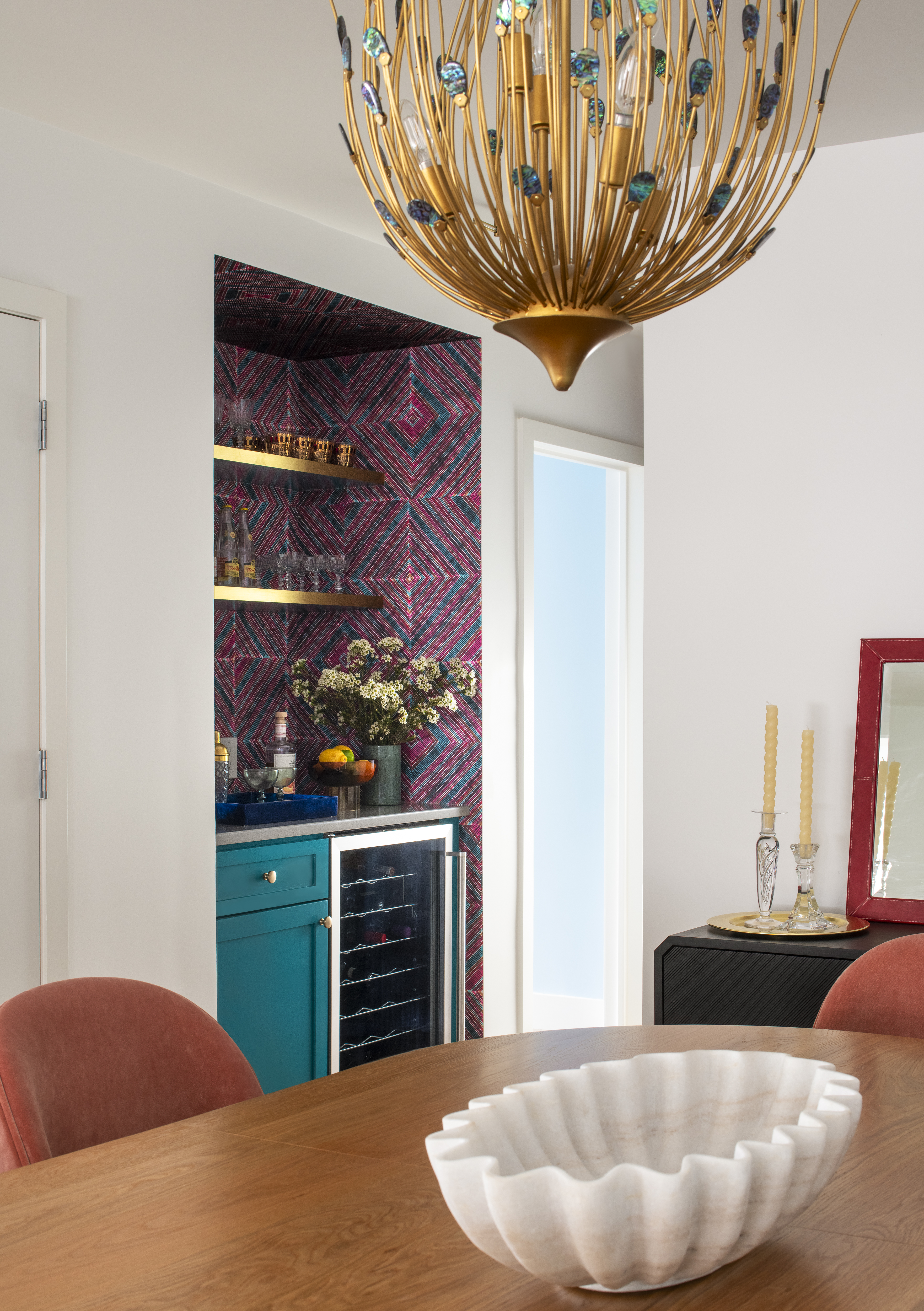 Dining area and bar view featuring a sculptural chandelier, patterned wallcovering, and teal cabinetry by K.A. Murphy Interiors.