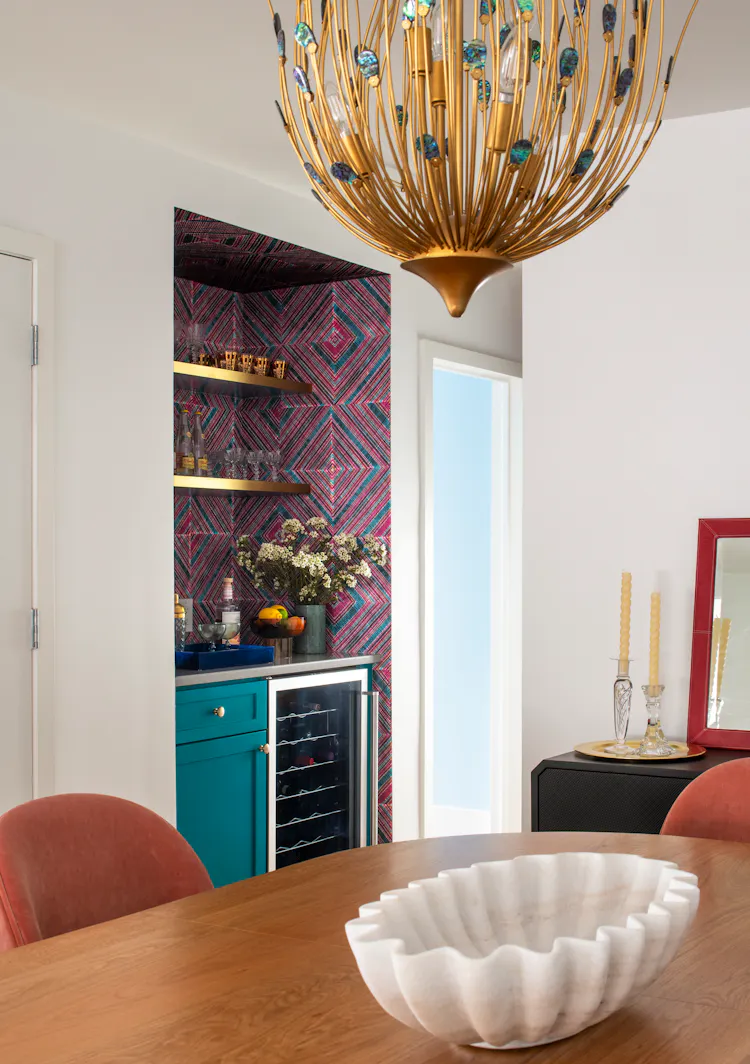 Dining area and bar view featuring a sculptural chandelier, patterned wallcovering, and teal cabinetry by K.A. Murphy Interiors.