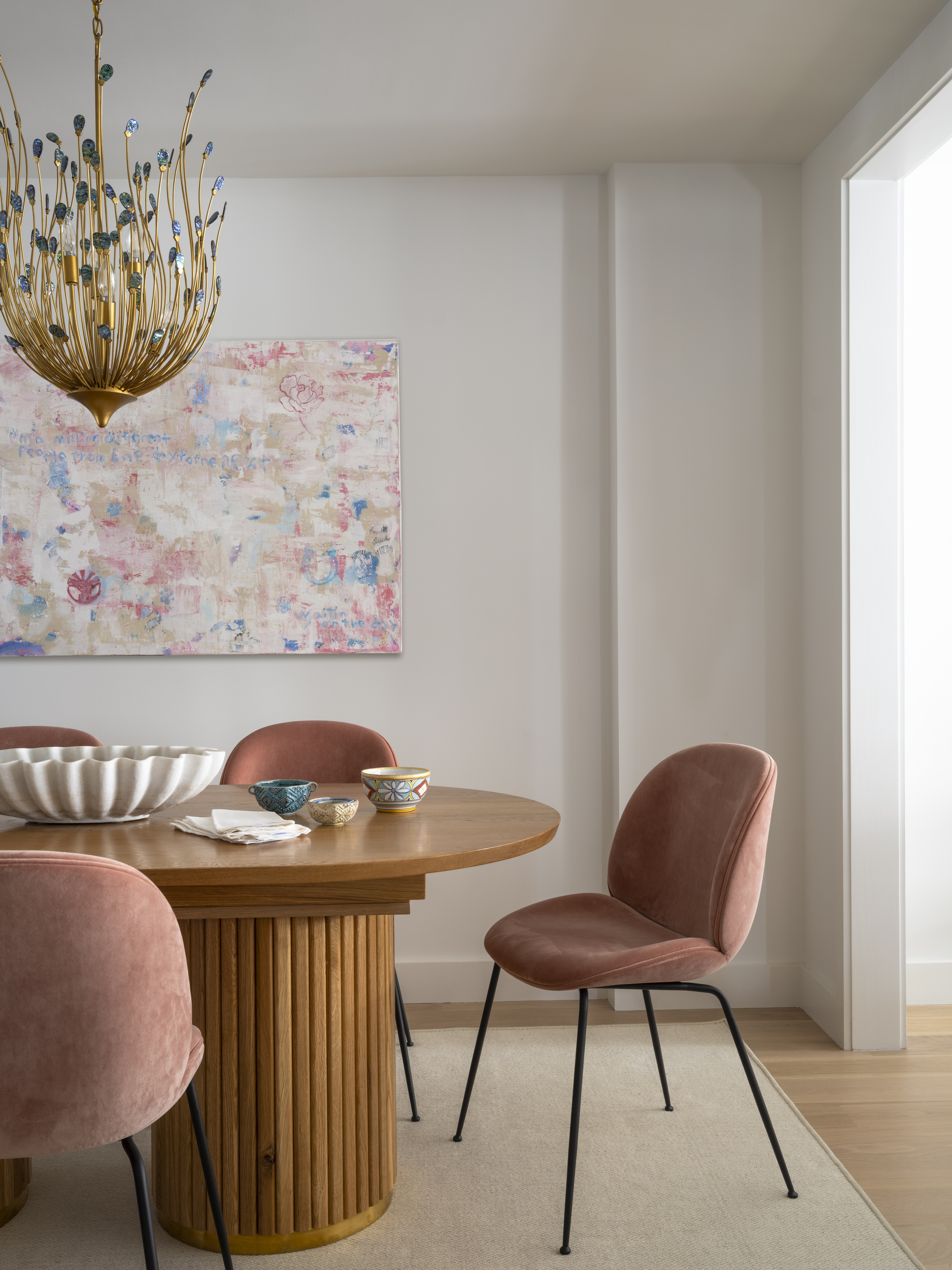 Dining room with a round wood table, blush velvet chairs, and statement chandelier by K.A. Murphy Interiors.