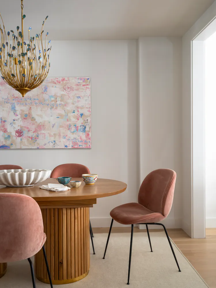 Dining room with a round wood table, blush velvet chairs, and statement chandelier by K.A. Murphy Interiors.