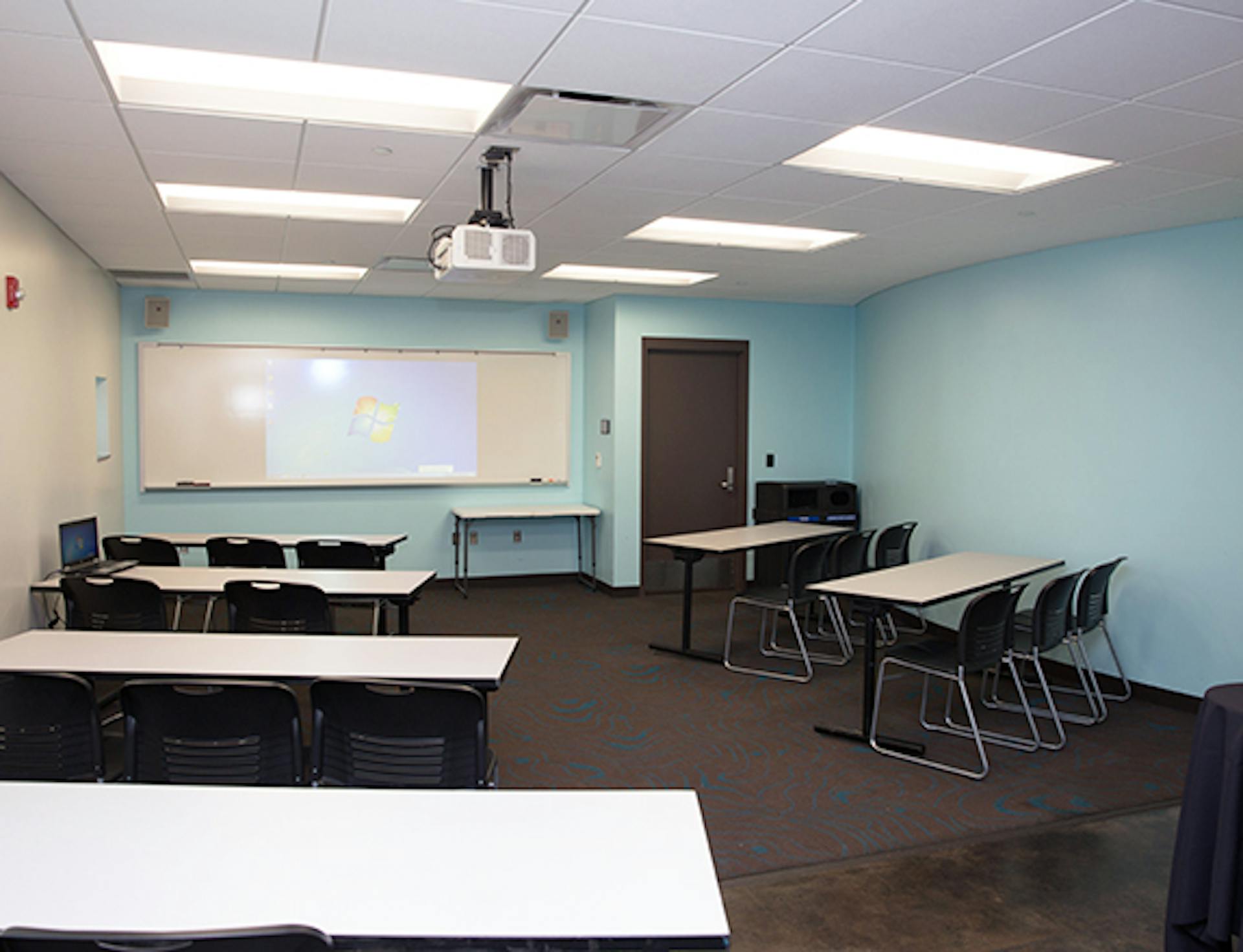 a classroom set six tables set up classroom style with chairs with a whiteboard at the front.