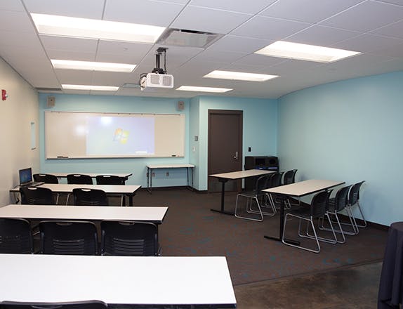 a classroom set six tables set up classroom style with chairs with a whiteboard at the front.