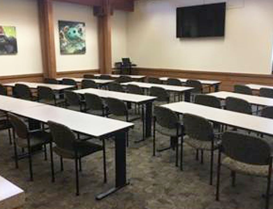 A conference room with 11 tables set classroom style with chairs and a large screen on wall