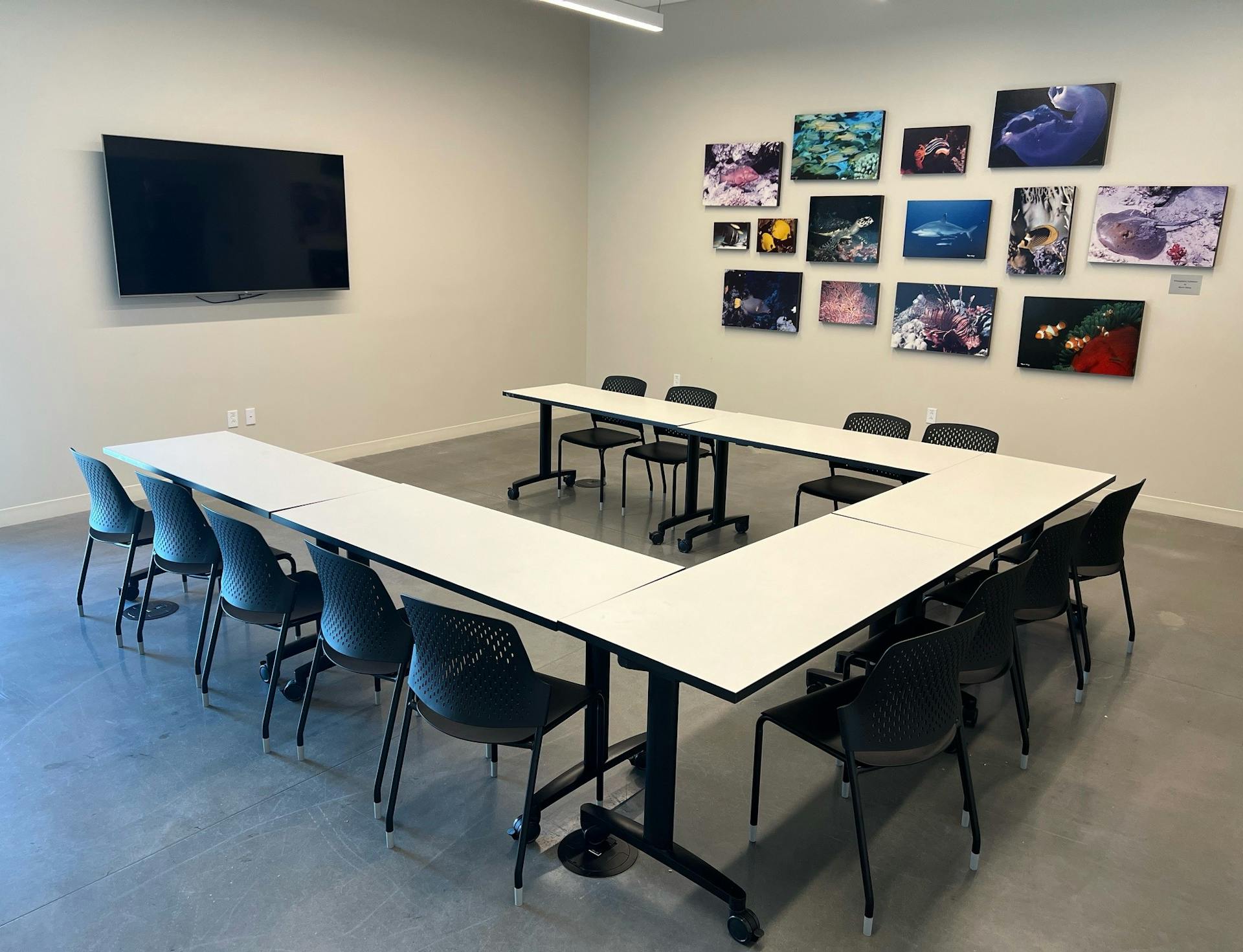 A confrence room with 5 tables and chairs and a large screen on the wall